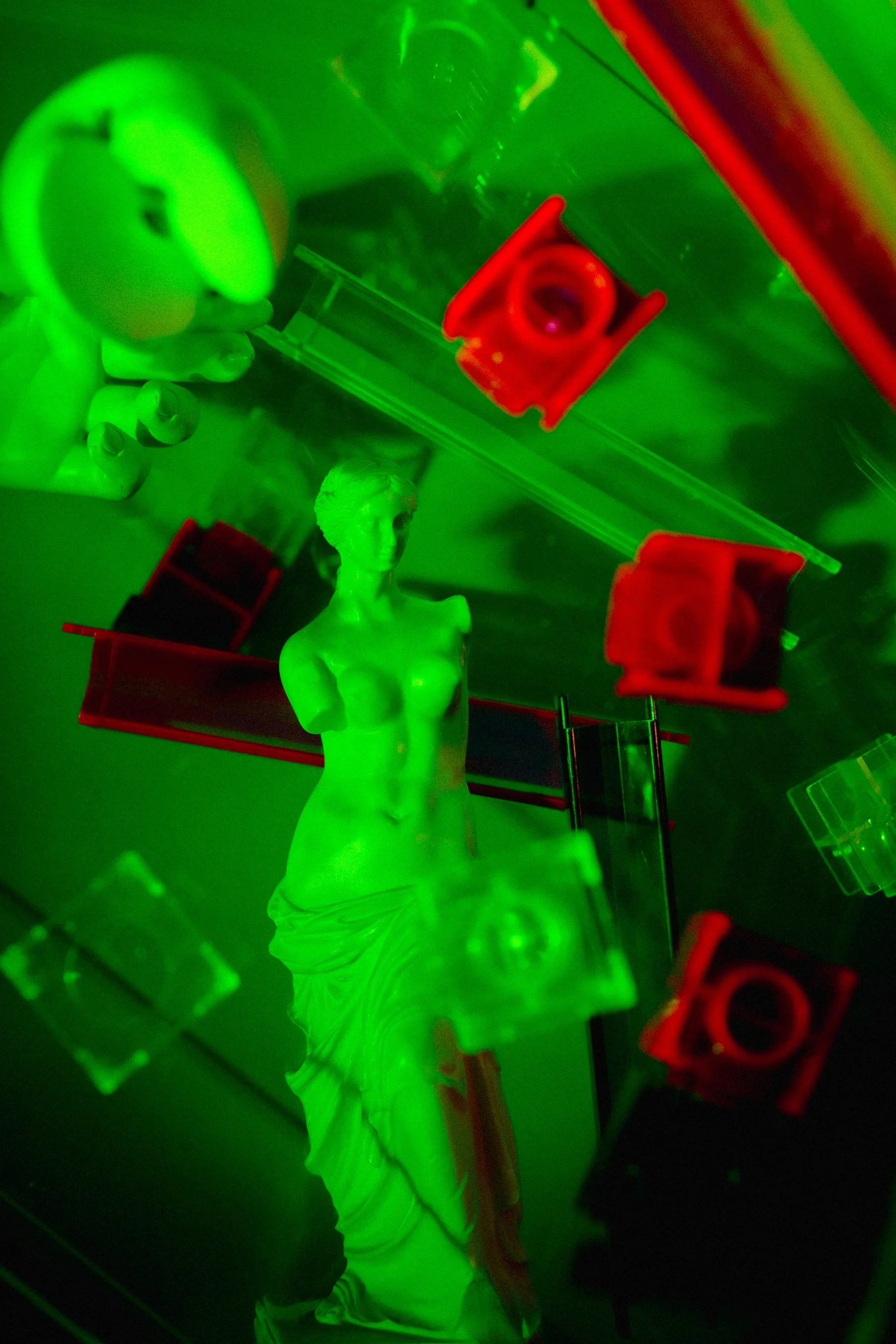 Green-lit display featuring a white statue of a woman with a draped gown, surrounded by various red and clear objects.