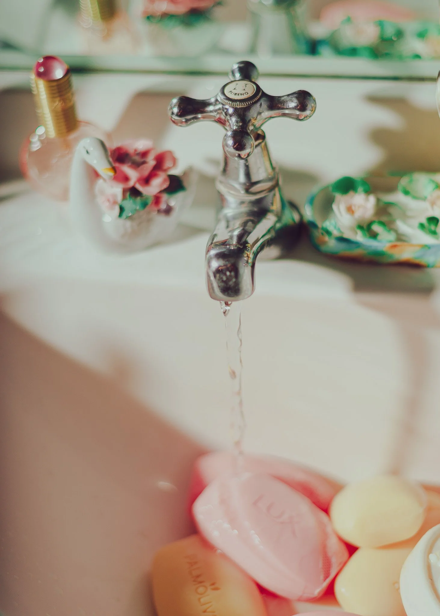 Close-up of a bathroom sink faucet with water dripping, with pastel-colored soap or bath bombs in the background.