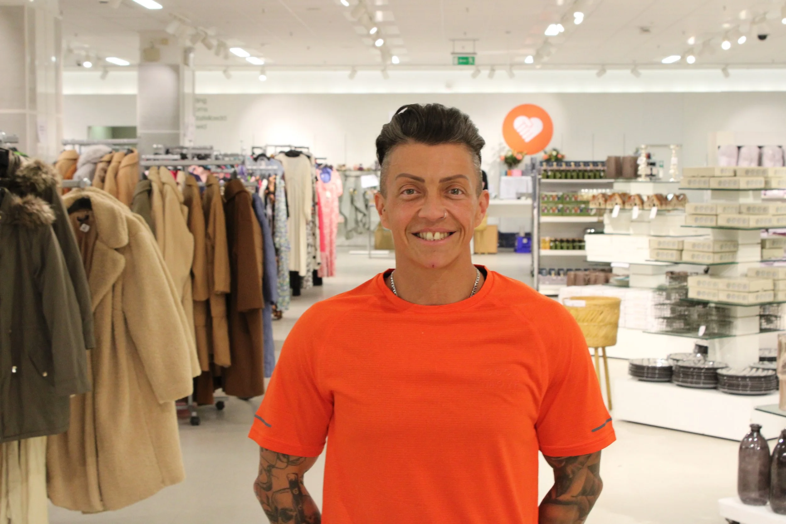 Man standing in a clothing store, surrounded by racks of clothes.