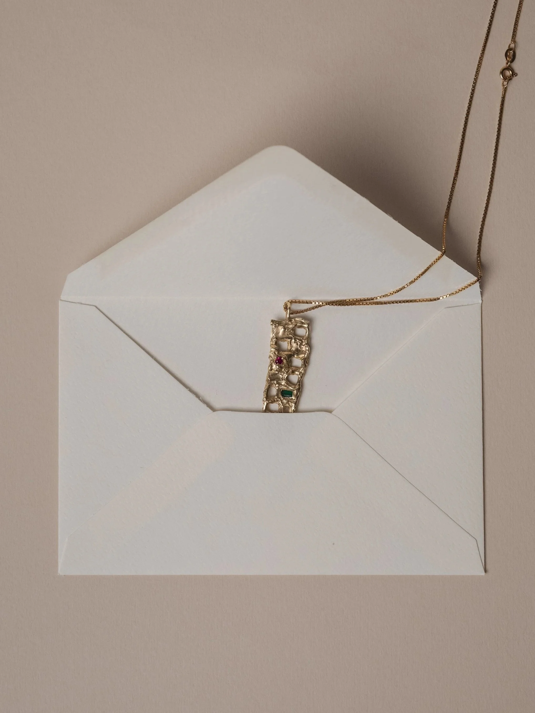 Collana con ciondolo e pietre zirconi colorati, posta su una busta bianca.