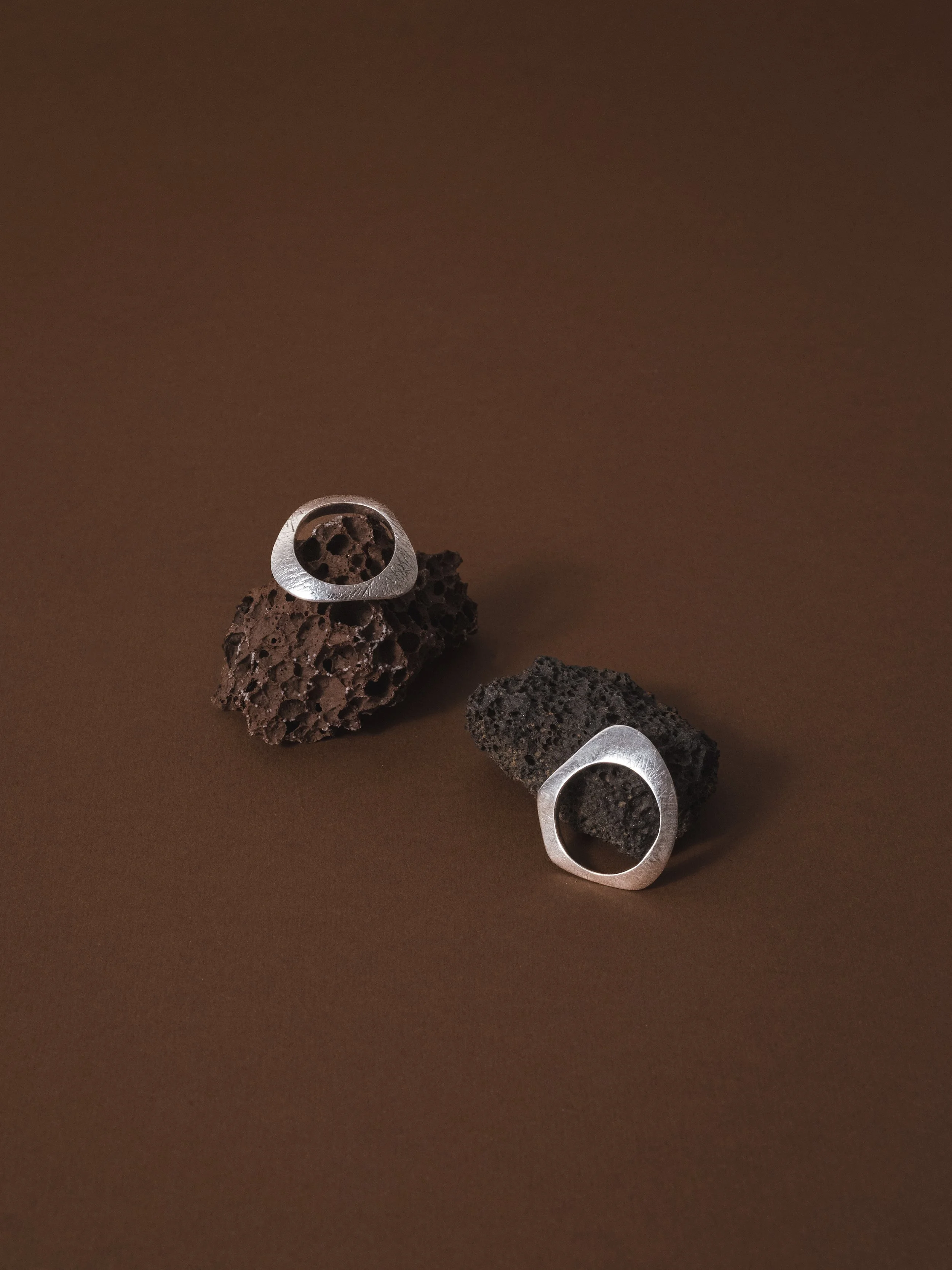 Due pezzi di roccia vulcanica con anelli metallici passanti, posizionati su uno sfondo marrone.