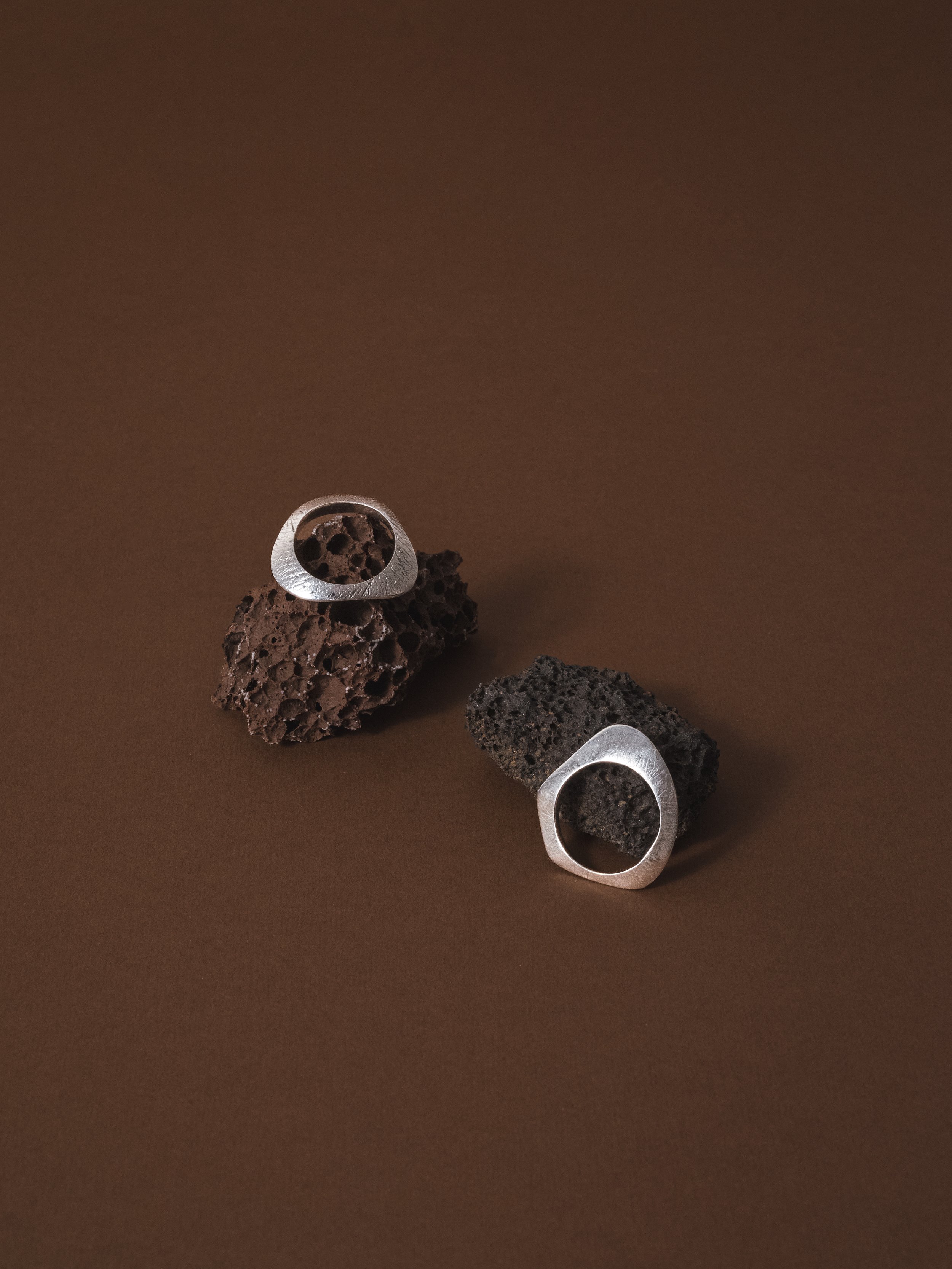 Anelli di metallo con forma geometrica e pezzi di roccia vulcanica nera sul fondo, su sfondo marrone
