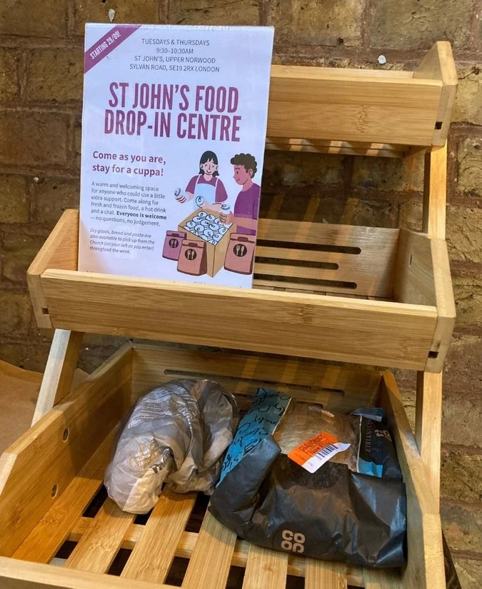 Wooden display shelf with a flyer for St John's Food Drop-In Centre, and a couple of pastry in paper and plastic wrappers on the bottom tray.