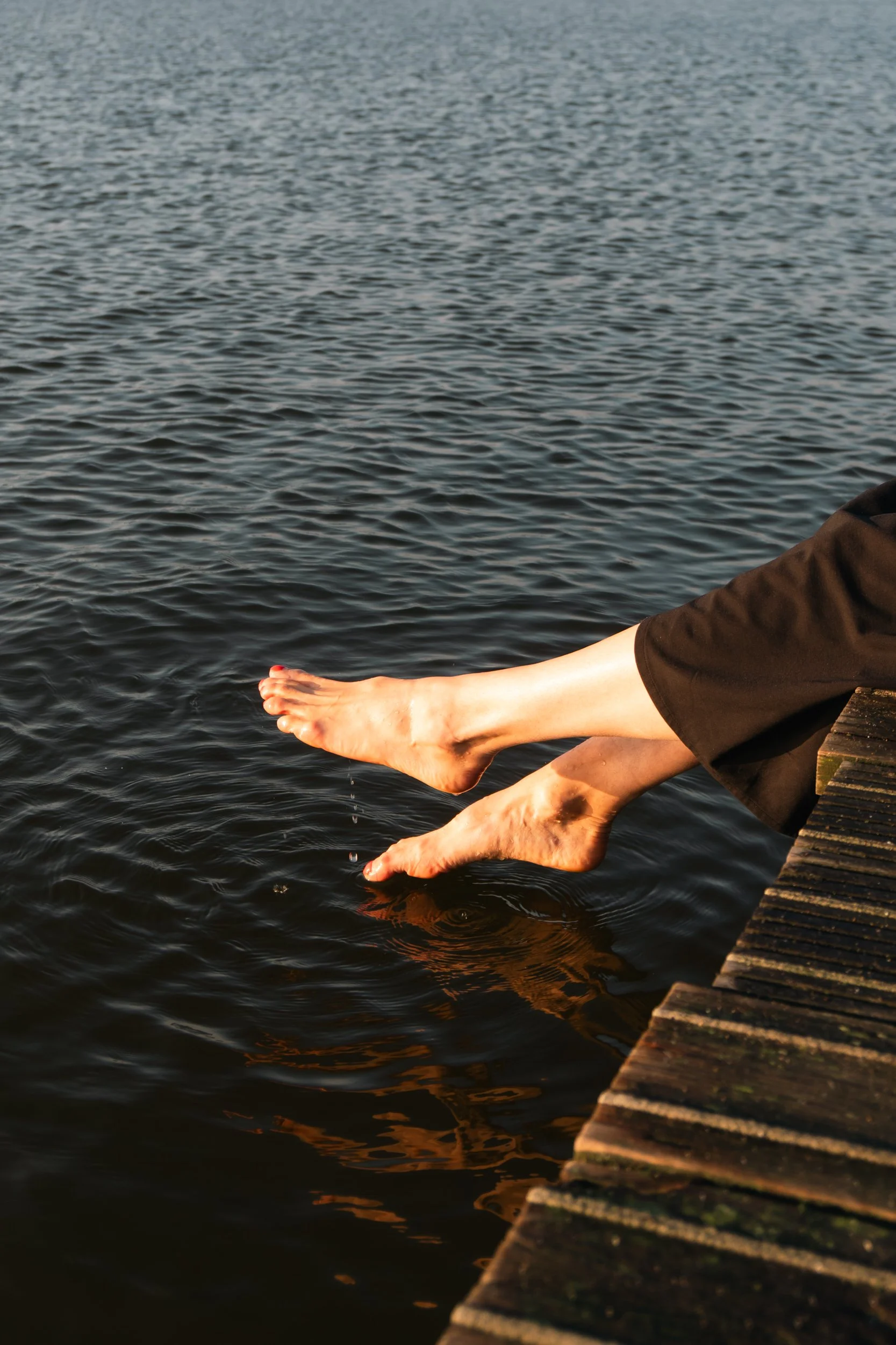 Personen die hun voeten in het water hangen vanaf een houten steiger.