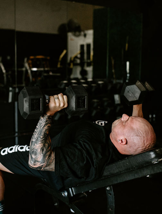 Liam lifting weights on a bench, holding dumbbells, in a gym setting.
