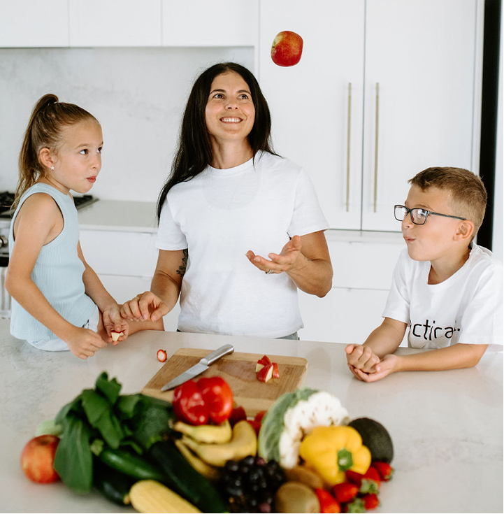 Tenille and her two children in a kitchen with assorted fruits and vegetables on the counter.