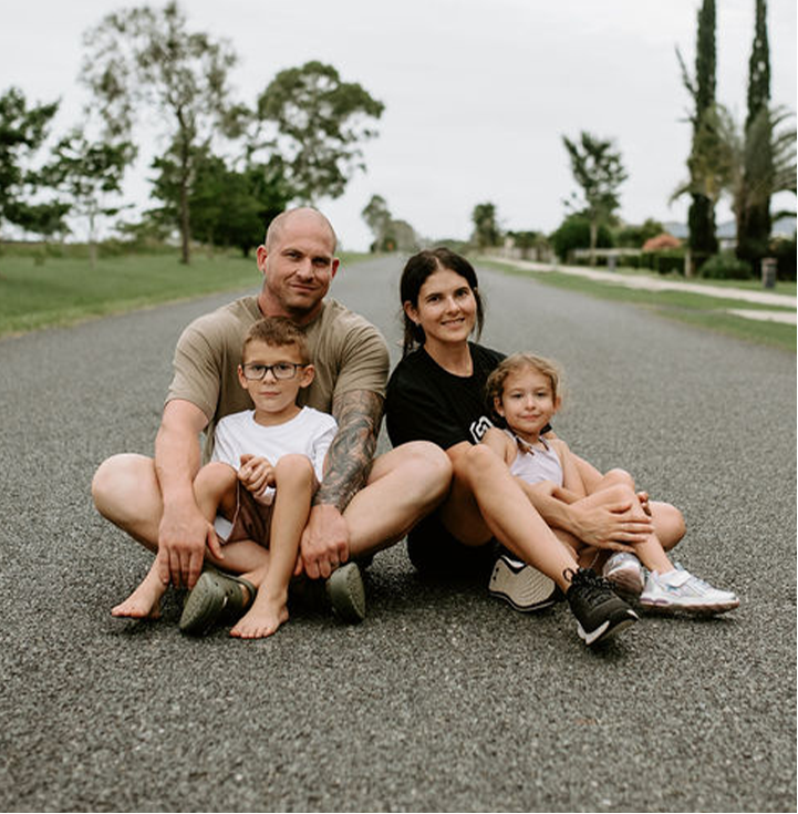 Tenille and Liam on a road, with their two children, with trees in the background.