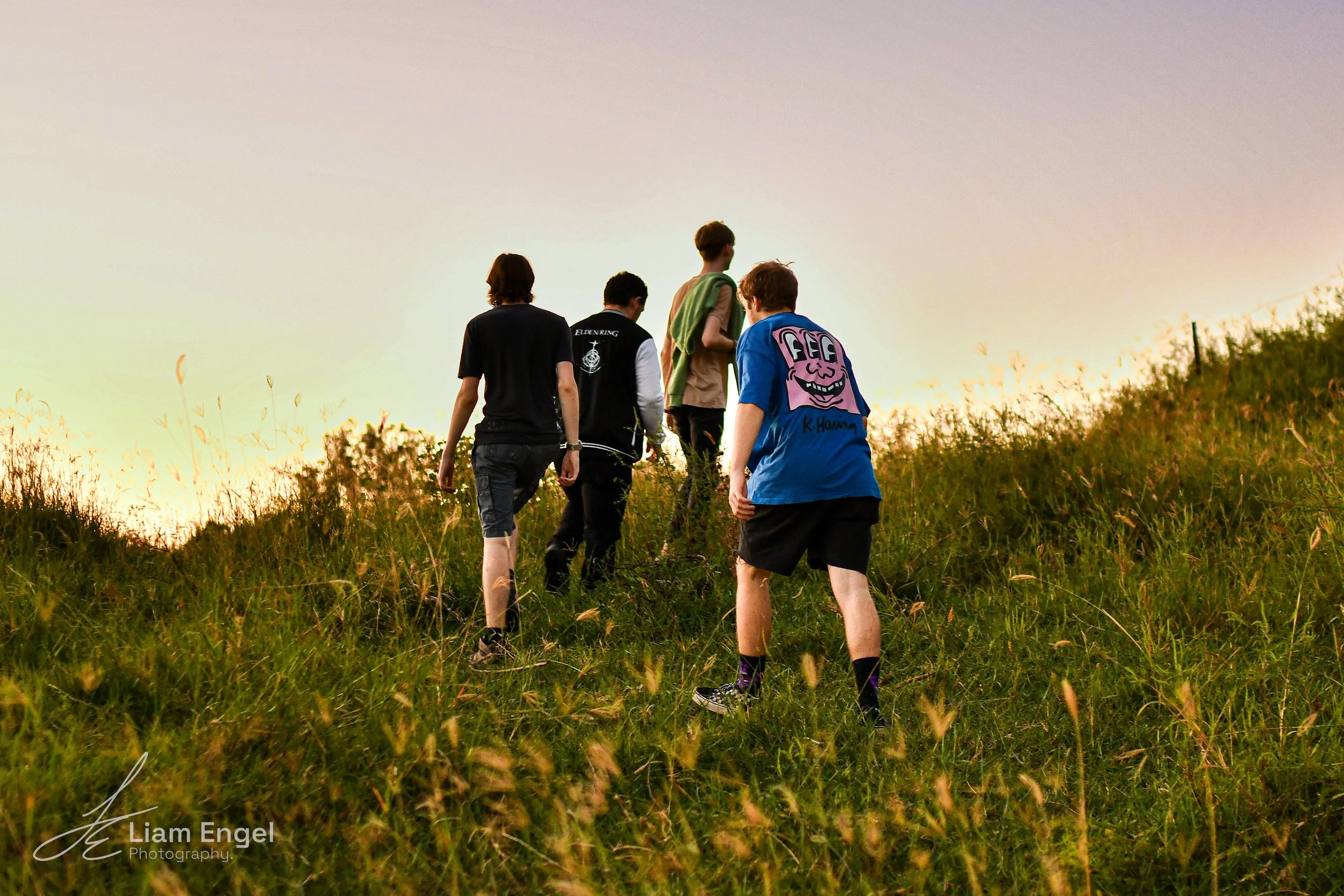 A group of five people hiking up a grassy hill during sunset.