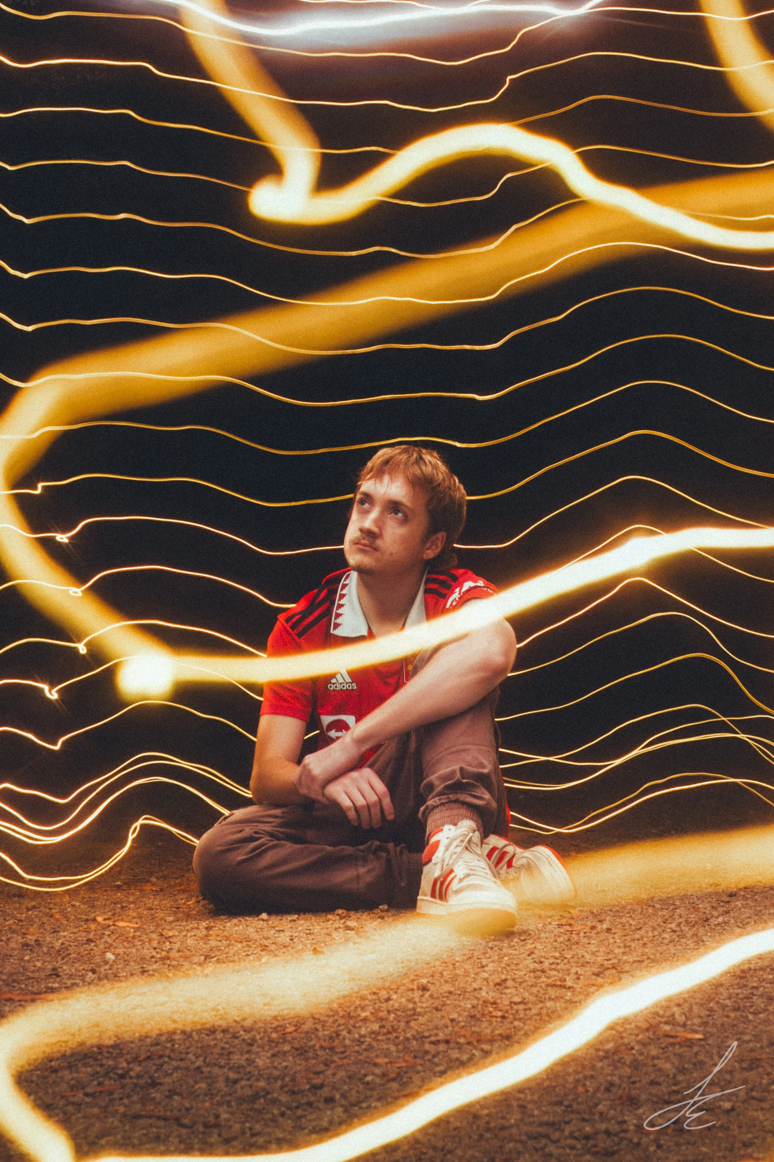 A young man sitting on the ground at night with swirling light trails around him.