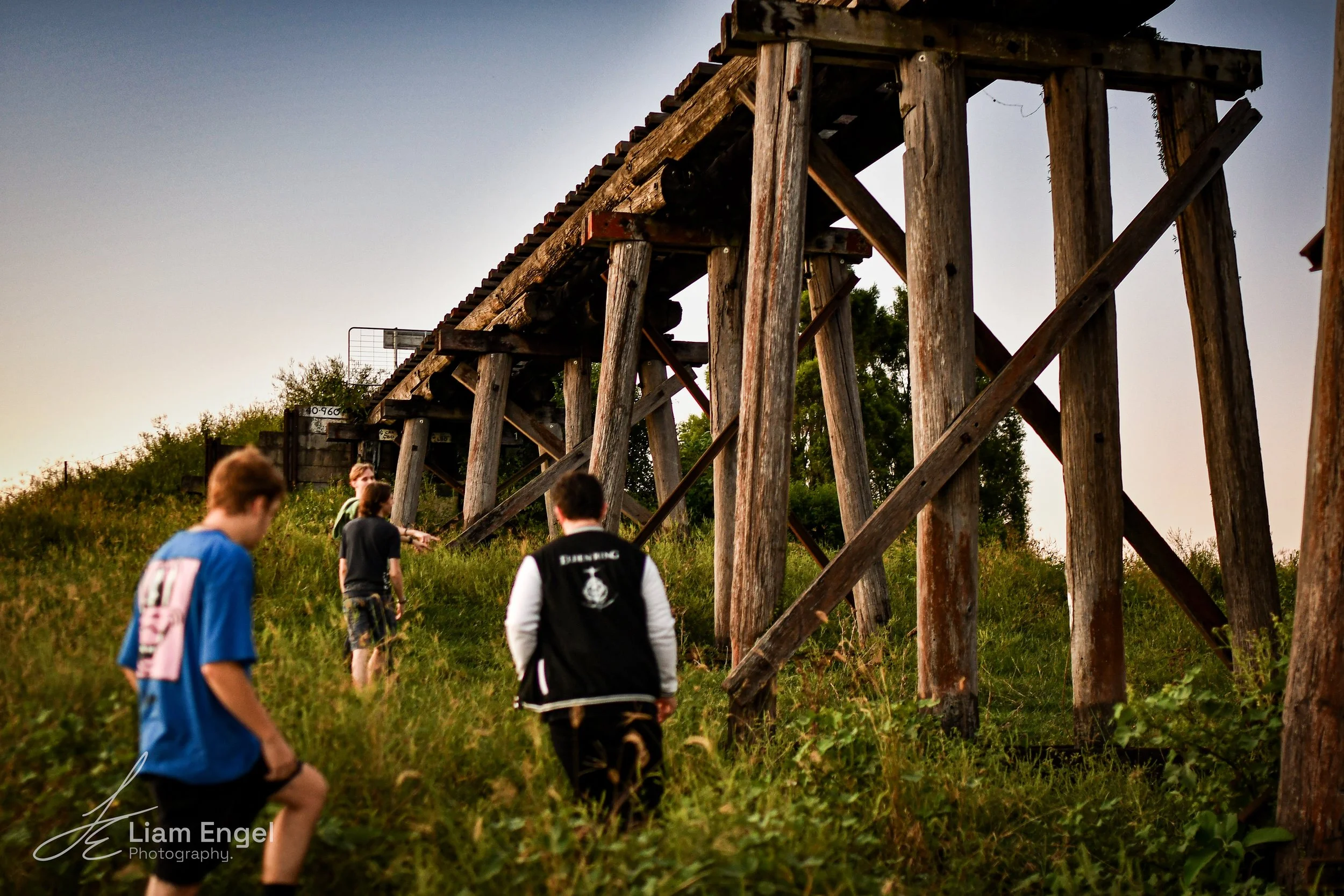 Four boys walking up a grassy hill under a wooden bridge or trestle cross.