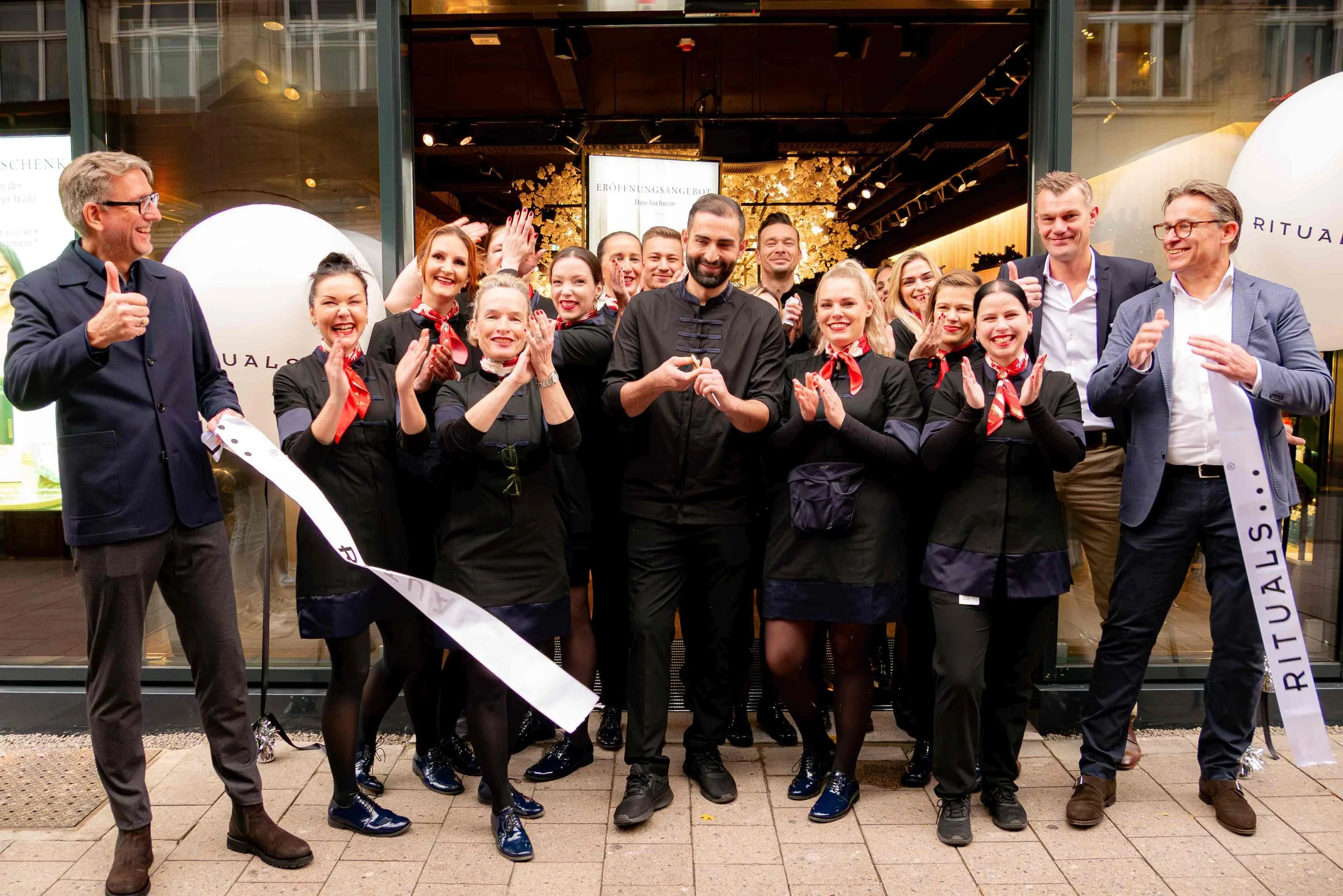 Eventfotografie in Hamburg und Umgebung von Klaudia Schmidt. Gruppe von Menschen, die vor dem Rituals-Geschäft cheerend und lachend posieren. Es handelt sich vermutlich um eine Feier oder Eröffnung.