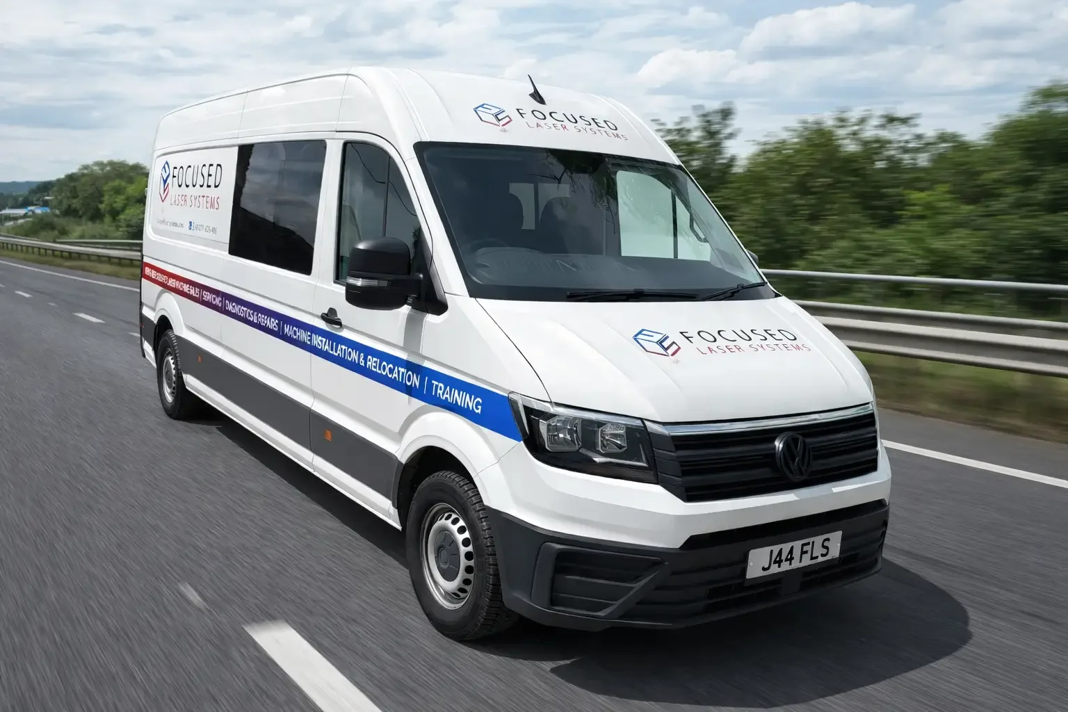 A white cargo van driving on a highway with a green hillside in the background.
