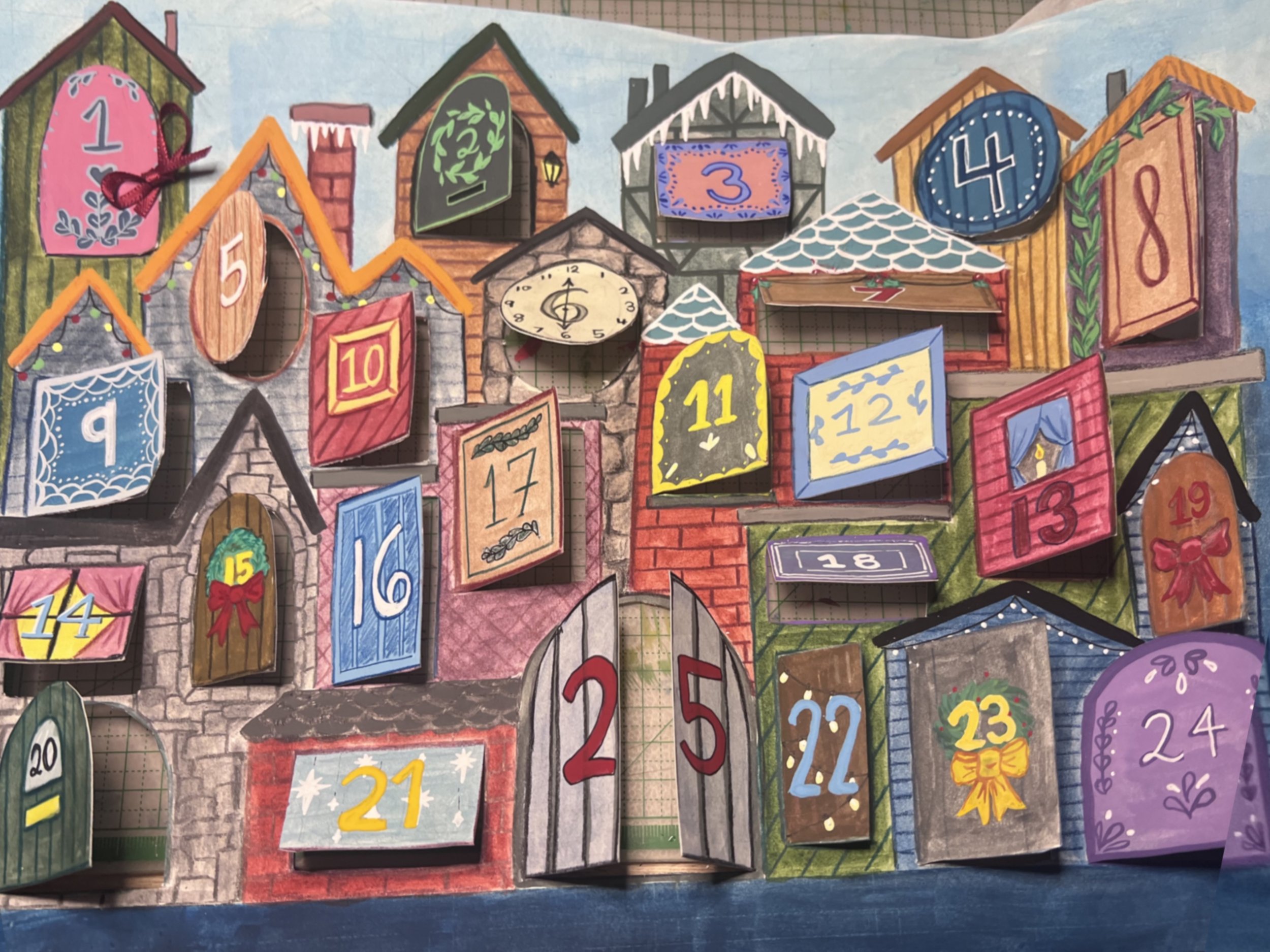 Colorful Christmas-themed advent calendar resembling a house with numbered doors from 1 to 24, some doors decorated with bows, snow, or patterns.