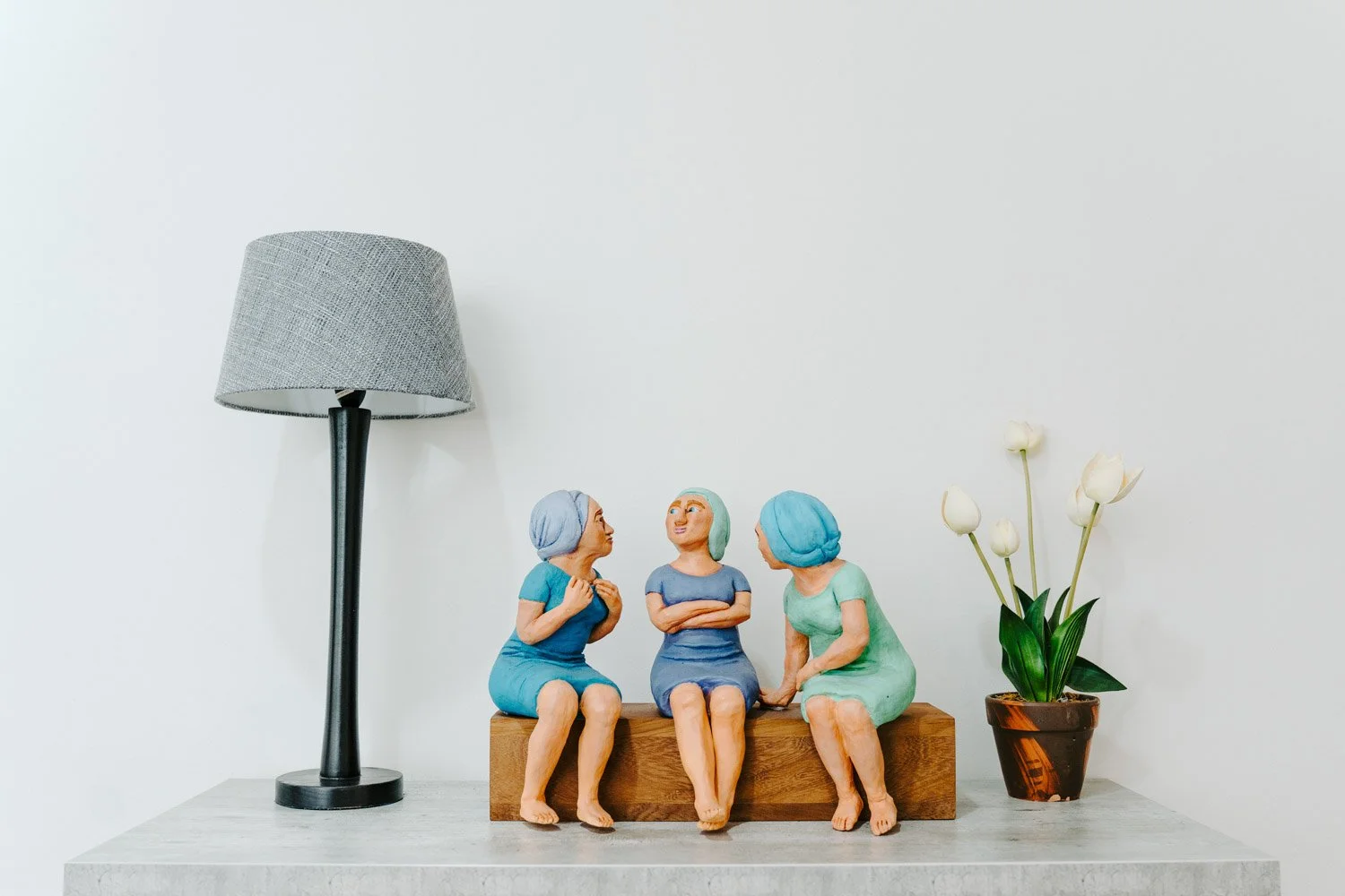 Dr Riette de Lauwere, Clinical Psychologist decor items in her office: Gray lamp, three female figurines in blue dresses on wooden block, potted white tulips on table.