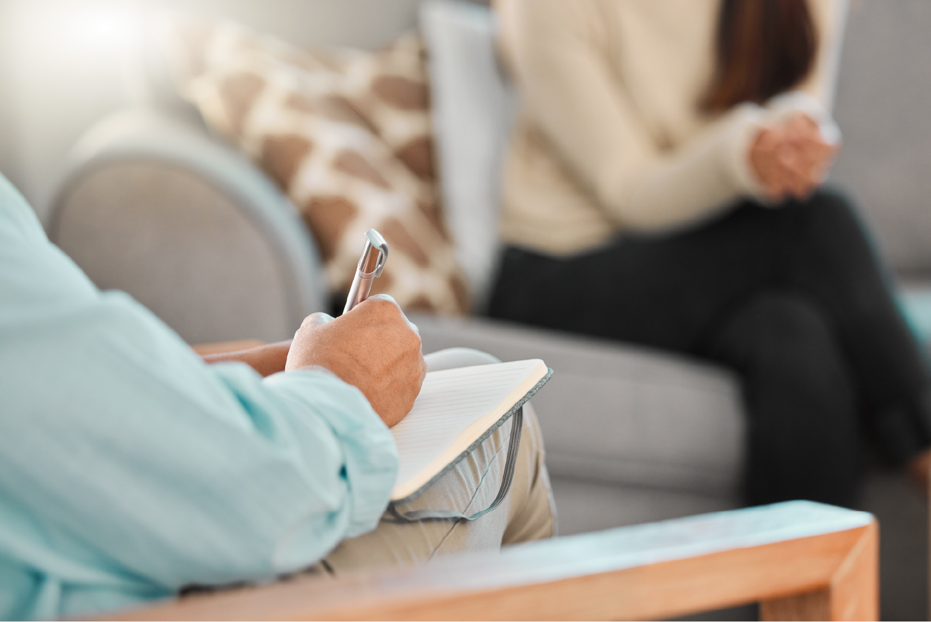 Dr Riette de Lauwere, Clinical Psychologist in session:  writing in notebook during counseling session with another person in the background on a couch.