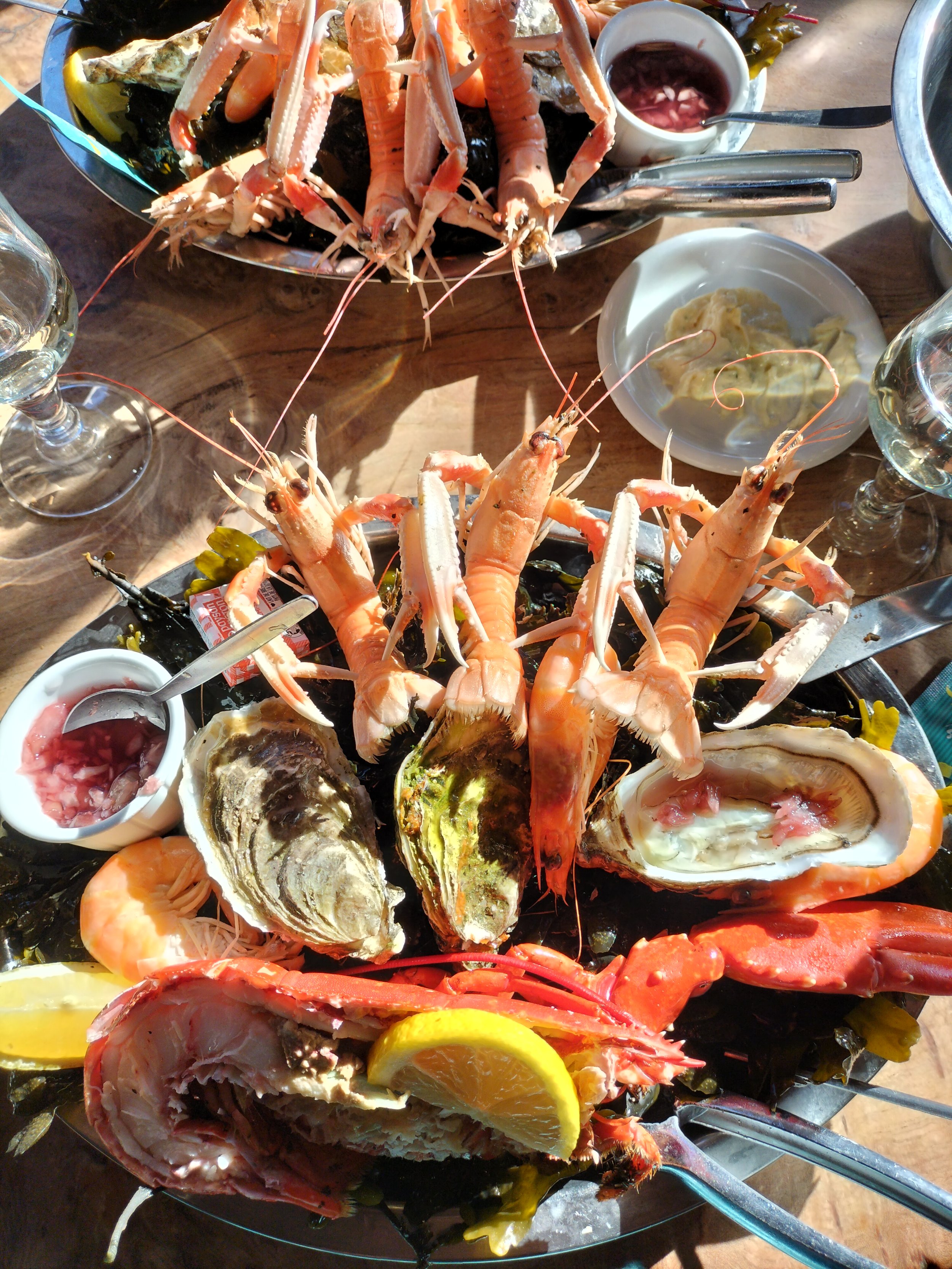 Seafood platter with prawns, oysters, and lobster, garnished with lemon slices, accompanied by sauce bowls and a glass of white wine.