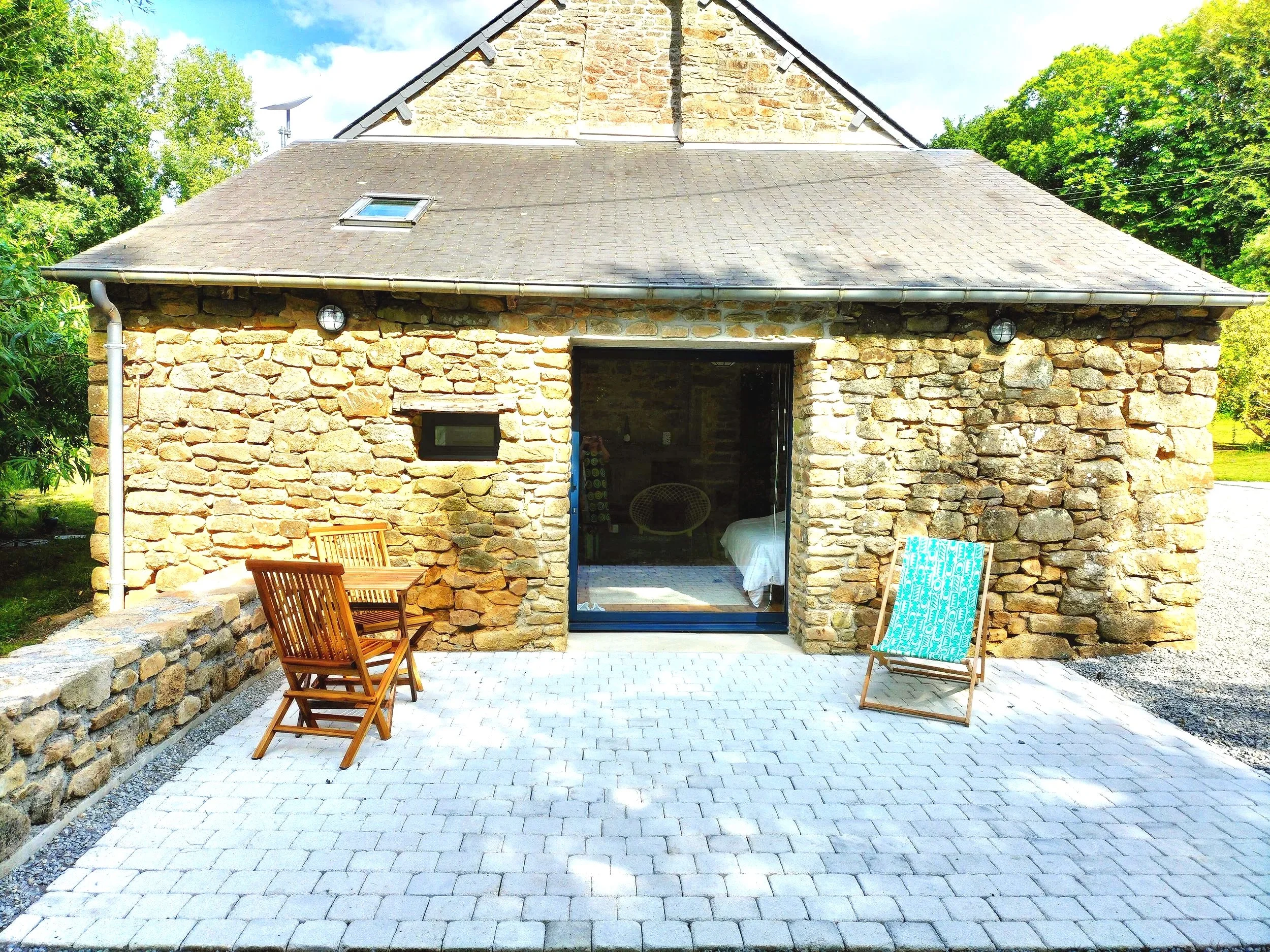 Interior of a rustic bedroom with stone walls, wooden flooring, a bed with white linens, and a glass sliding door.