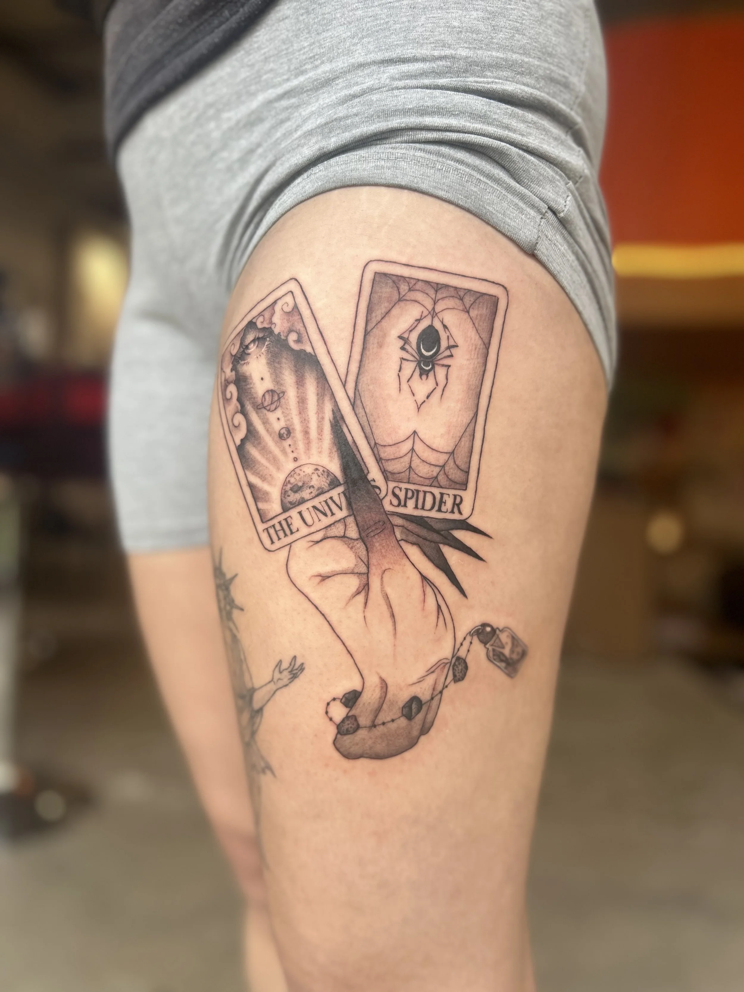 Tatouage représentant deux cartes de tarot, une avec un serpent et l'autre avec une araignée, accompagnées d'une main dans une position spécifique. Texte sur la tatouage : "The Universe Spider".
