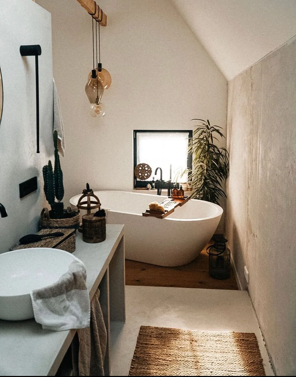 Moderner Badezimmerbereich mit freistehender Badewanne am Fenster, Pflanzen, Handtüchern, Dekorationsgegenständen und warmem Licht.