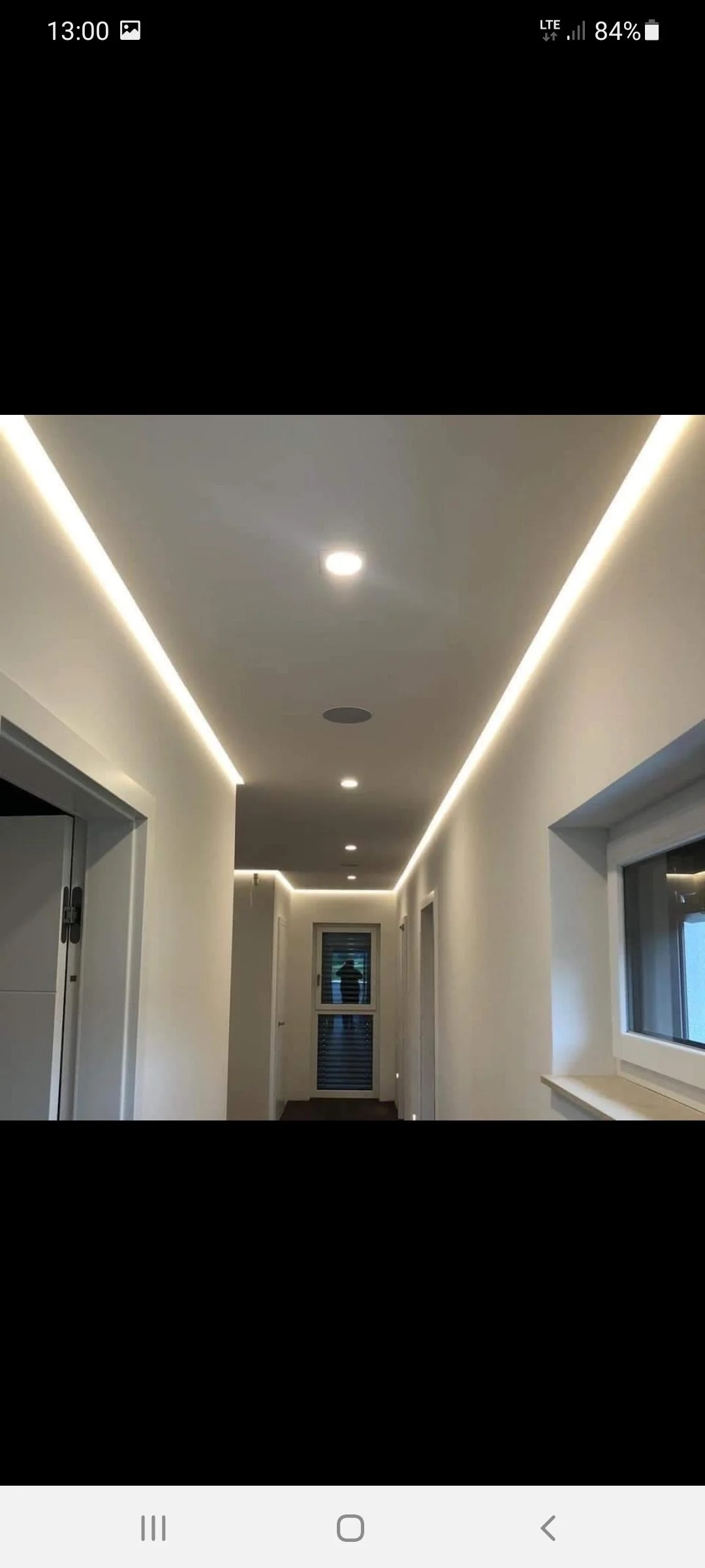 Ein heller Flur mit weißen Wänden und LED-Deckenbeleuchtung, Fenstern auf der rechten Seite und einer Tür am Ende des Gangs.