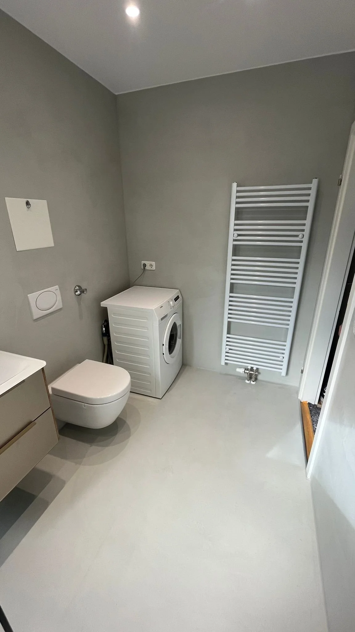 Ein Badezimmer mit einem wandhängenden WC, einer Waschmaschine, einem weißen Handtuchheizkörper und grauen Wänden.