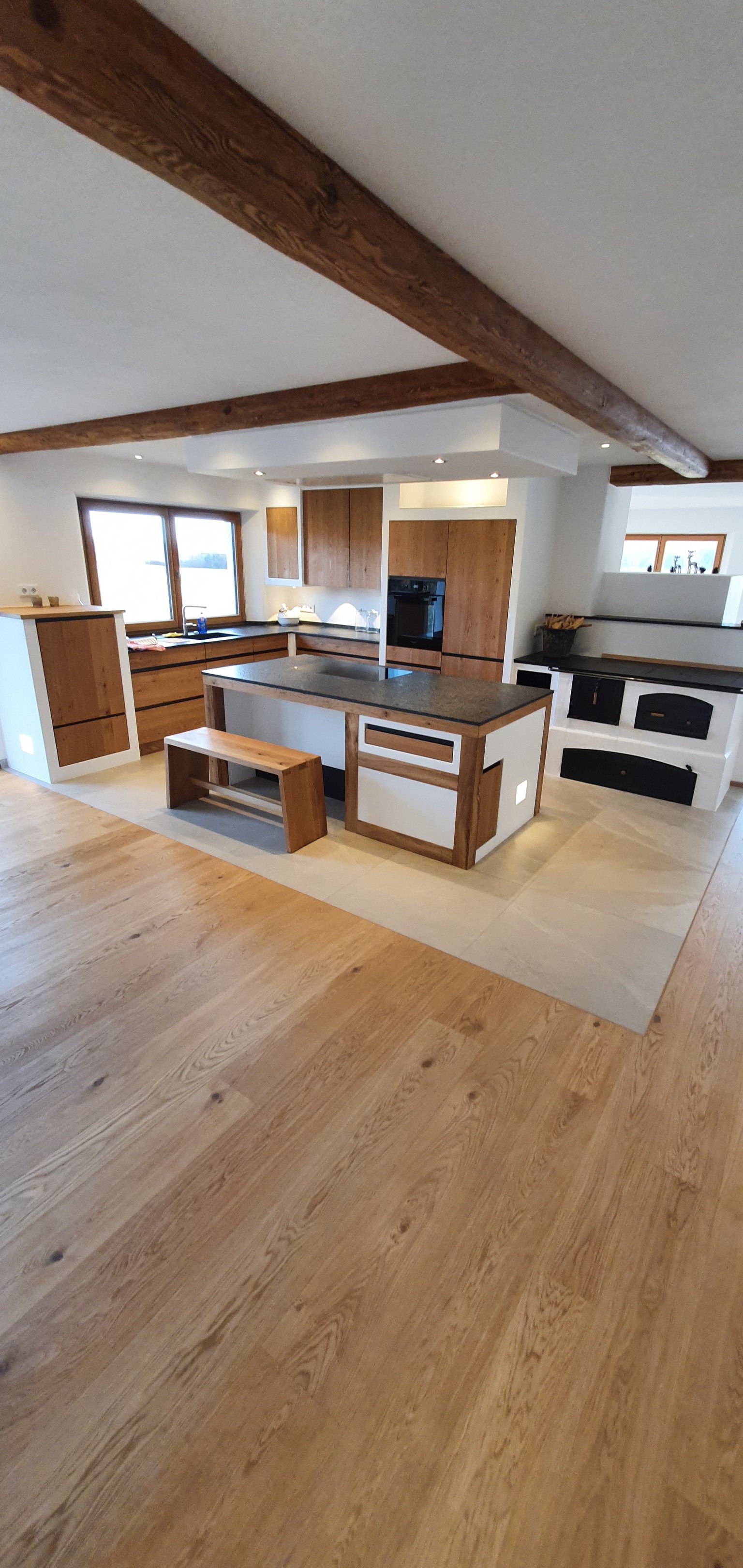 Moderne offene Küche mit Holzelementen, einem Küchenblock, Ofen, Fenster und hellen Holzboden.