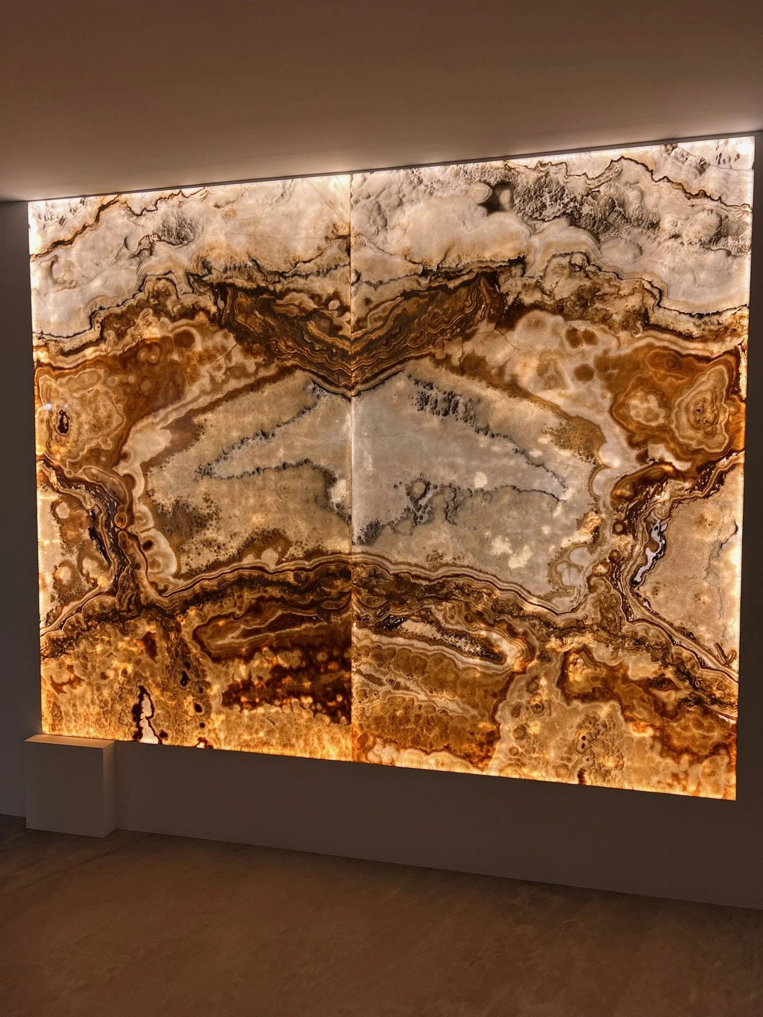 Ein beleuchtetes Wandbild aus durchscheinendem Onyx mit Braun-, Grau- und Beigetönen und natürlichen Mustern.