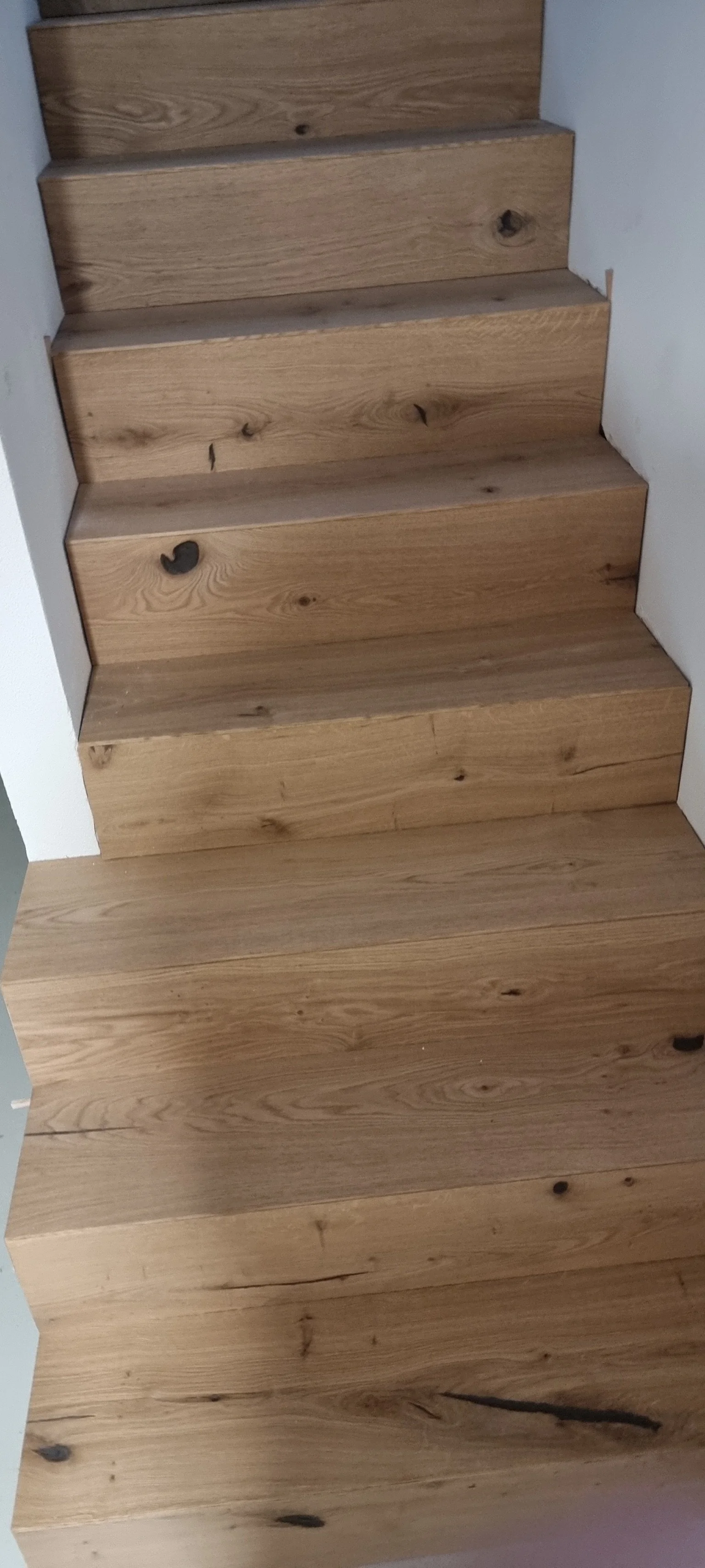 Holztreppenstufen mit sichtbaren Maserungen und Knorren, eingebaut zwischen weißen Wänden.