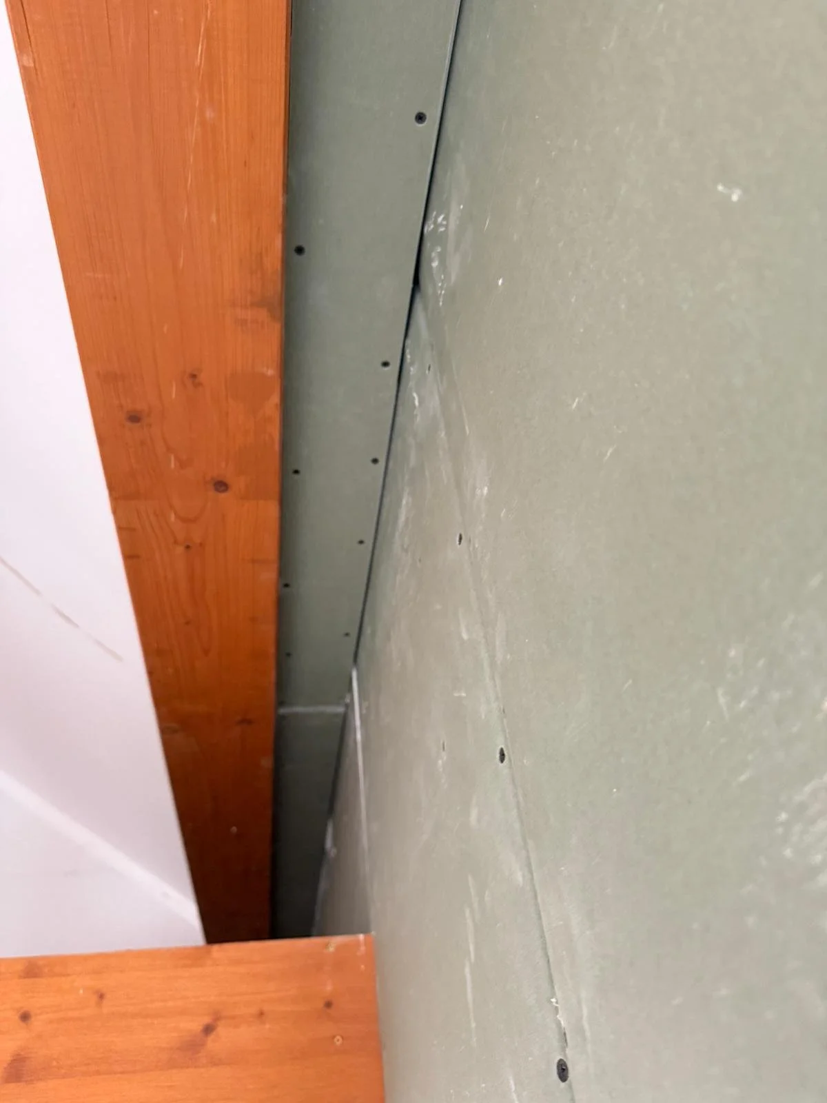 Das Foto zeigt eine Unterschrank-Bodenplatte, die auf einem Boden liegt. Die Platte besteht aus Metall, ist grau und hat mehrere Befestigungslöcher. Der Boden ist grünlich und an einer Seite sind Holzwände oder -leisten sichtbar.