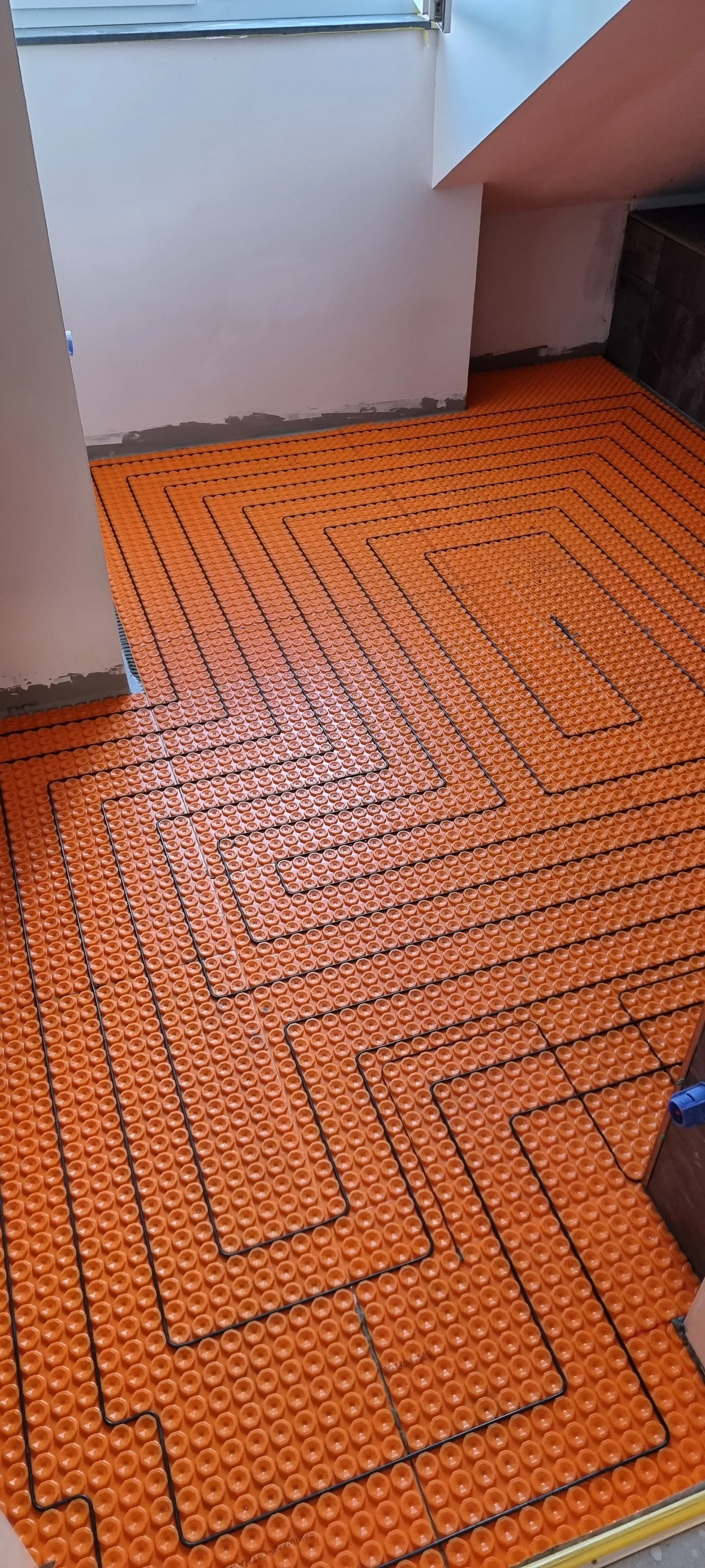 Installation einer Fußbodenheizung mit orangefarbenen Heizrohren im Raum.