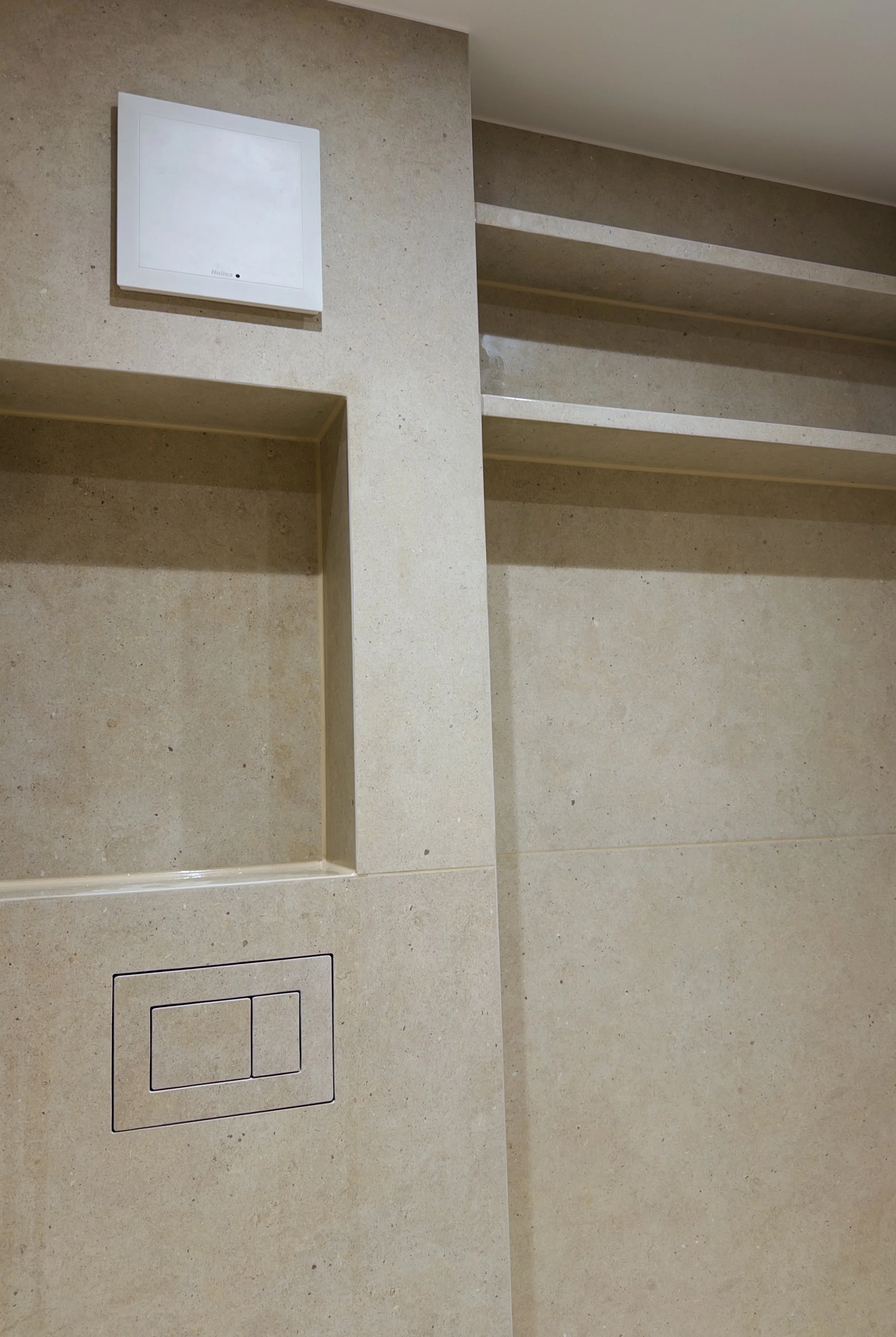 Ein beige gefliestes Badezimmer mit einer eingebauten Nische, einer Spülkastenabdeckung und einem weißen elektronischen Steuergerät an der Wand.