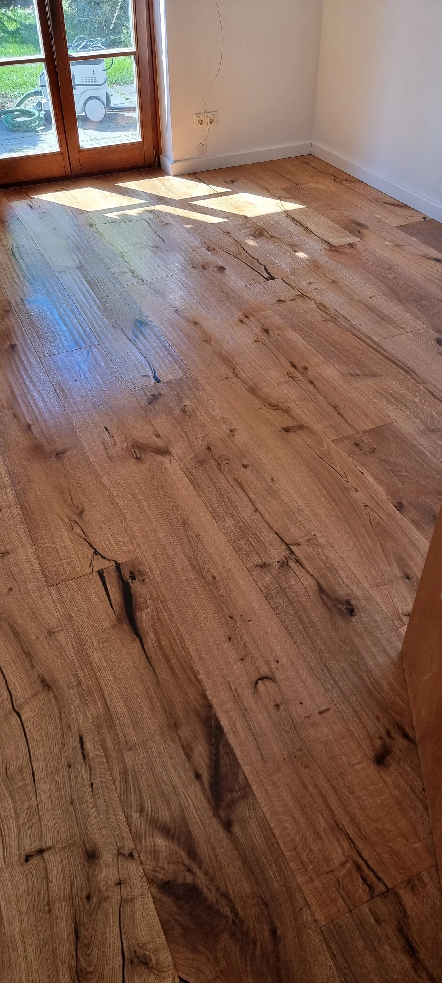 Hellbraune Holzdielenboden in einem Raum mit Glas-Schiebetür, teilweise im Sonnenlicht.