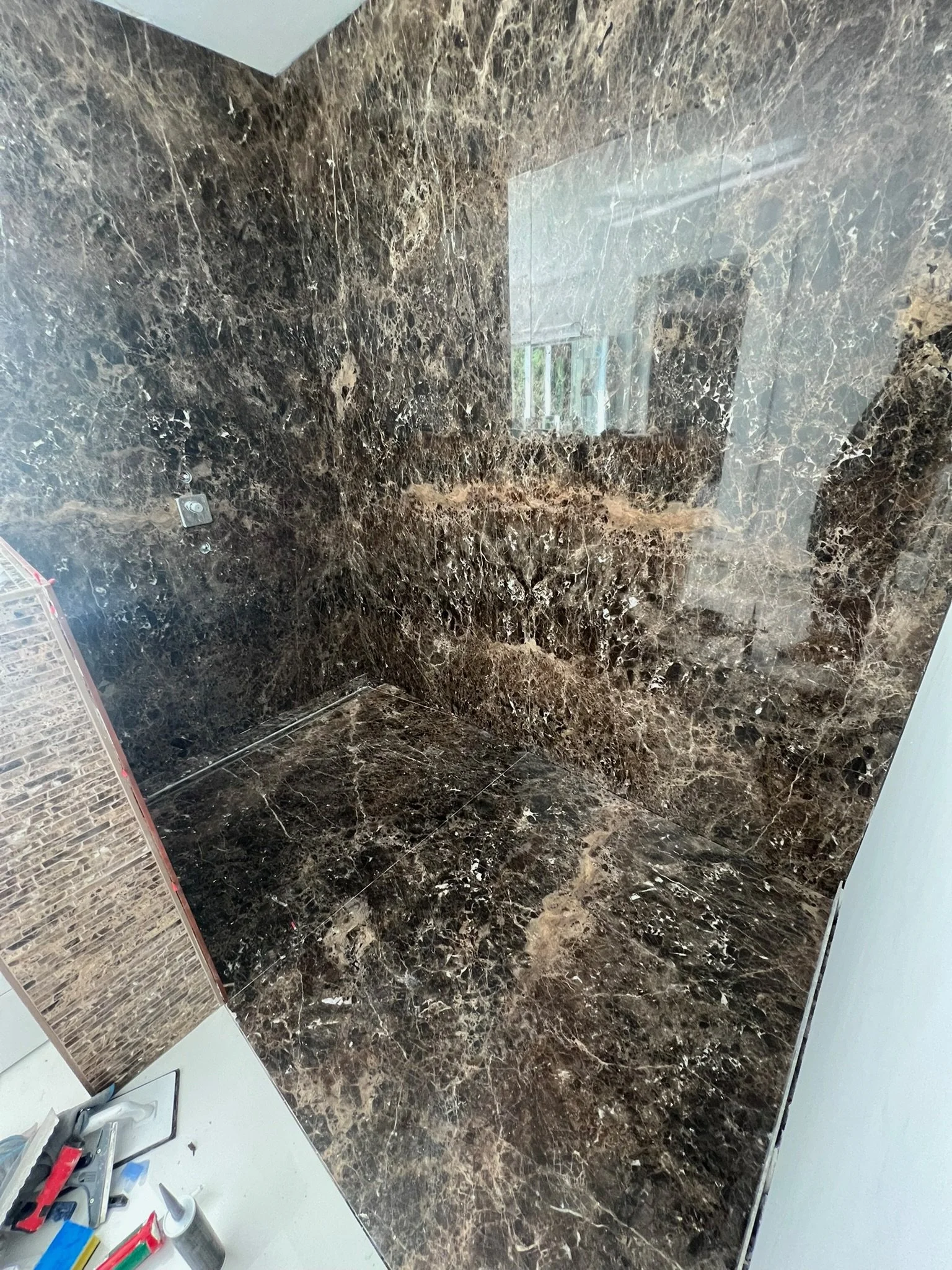 Innenansicht eines Badezimmers mit dunklem, braun schimmerndem Marmor, ohne sichtbare Armaturen.