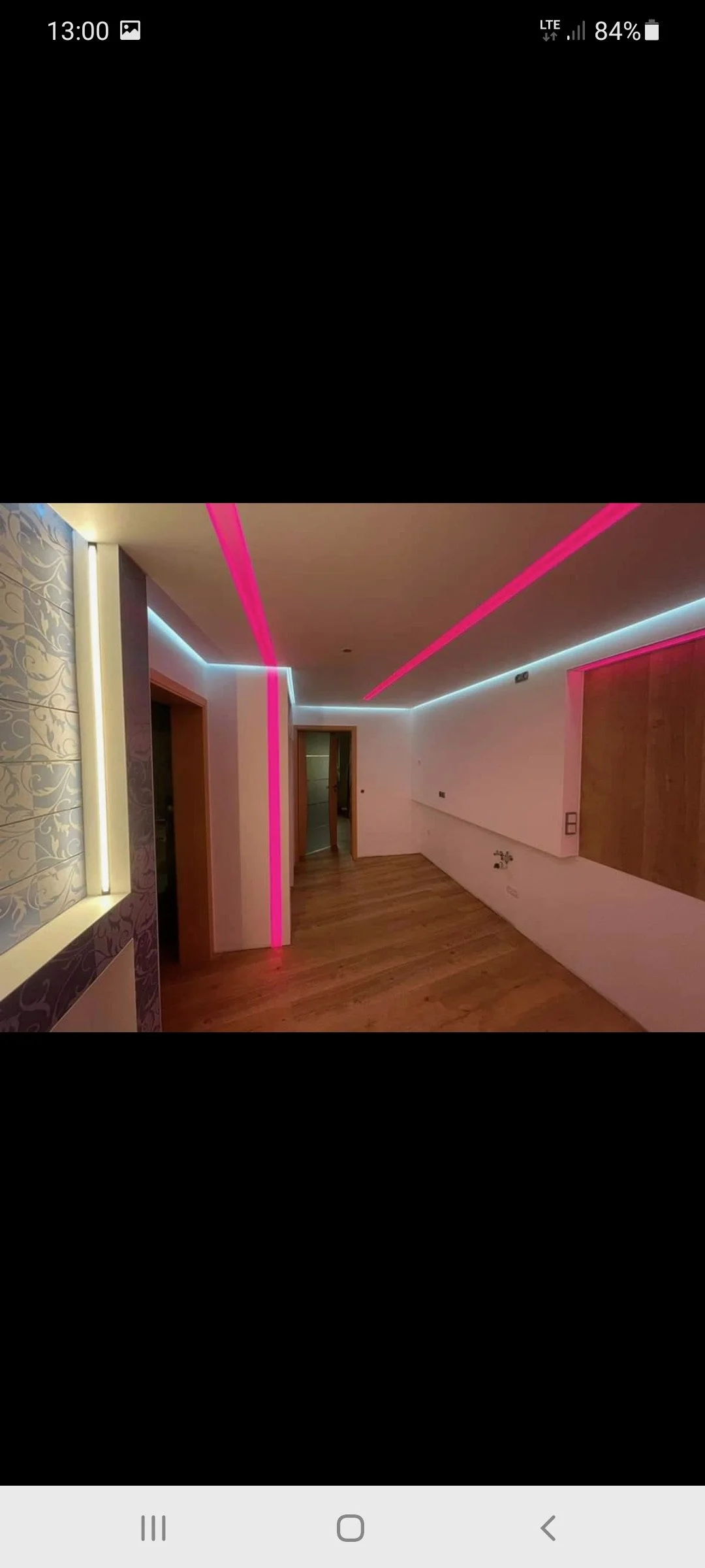 Ein Zimmer mit moderner Beleuchtung, inklusive LED-Streifen in Pink und Weiß, auf Holzfußboden, mit teilweise gestalteten Wänden.