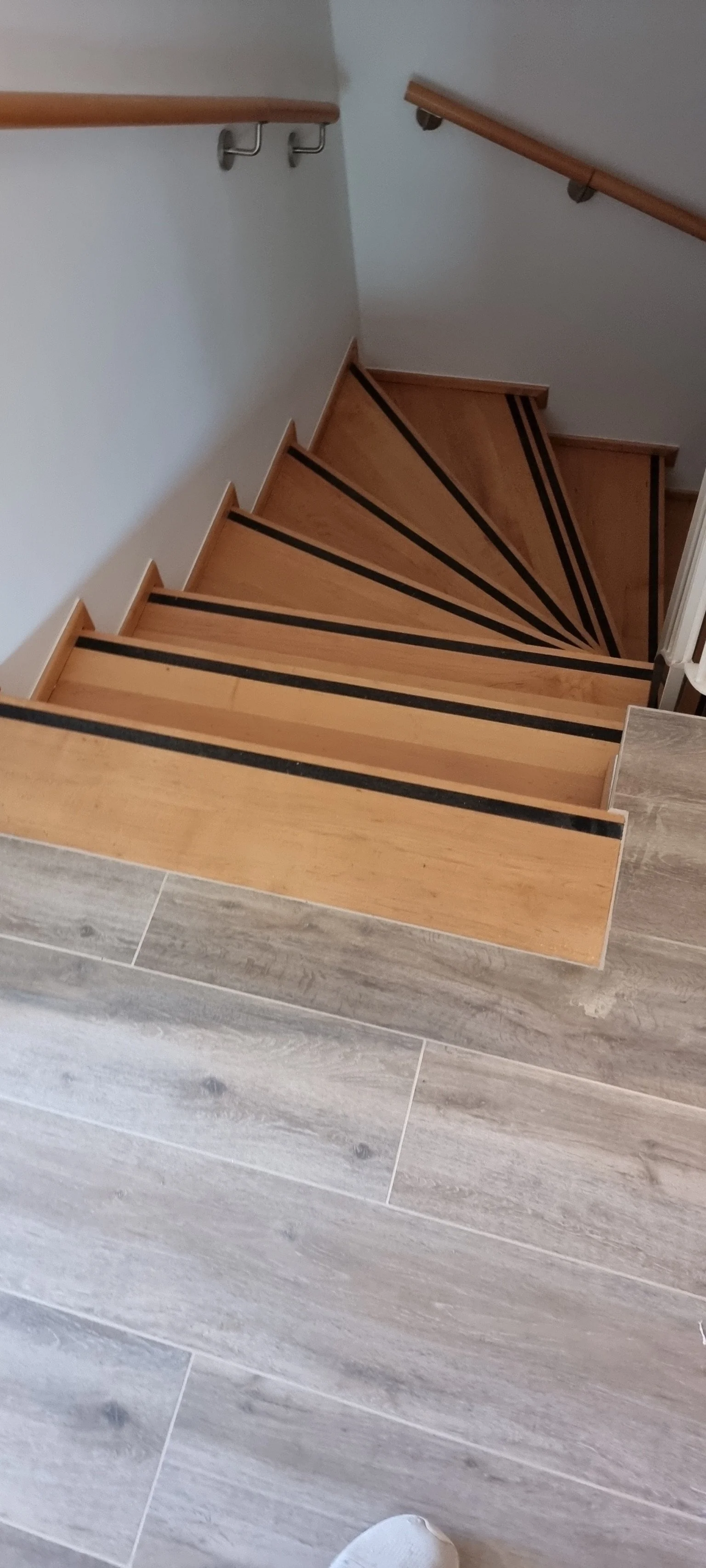 Holztreppe mit rutschfesten schwarzen Streifen, führend nach unten, mit Holzhandläufen an beiden Seiten.