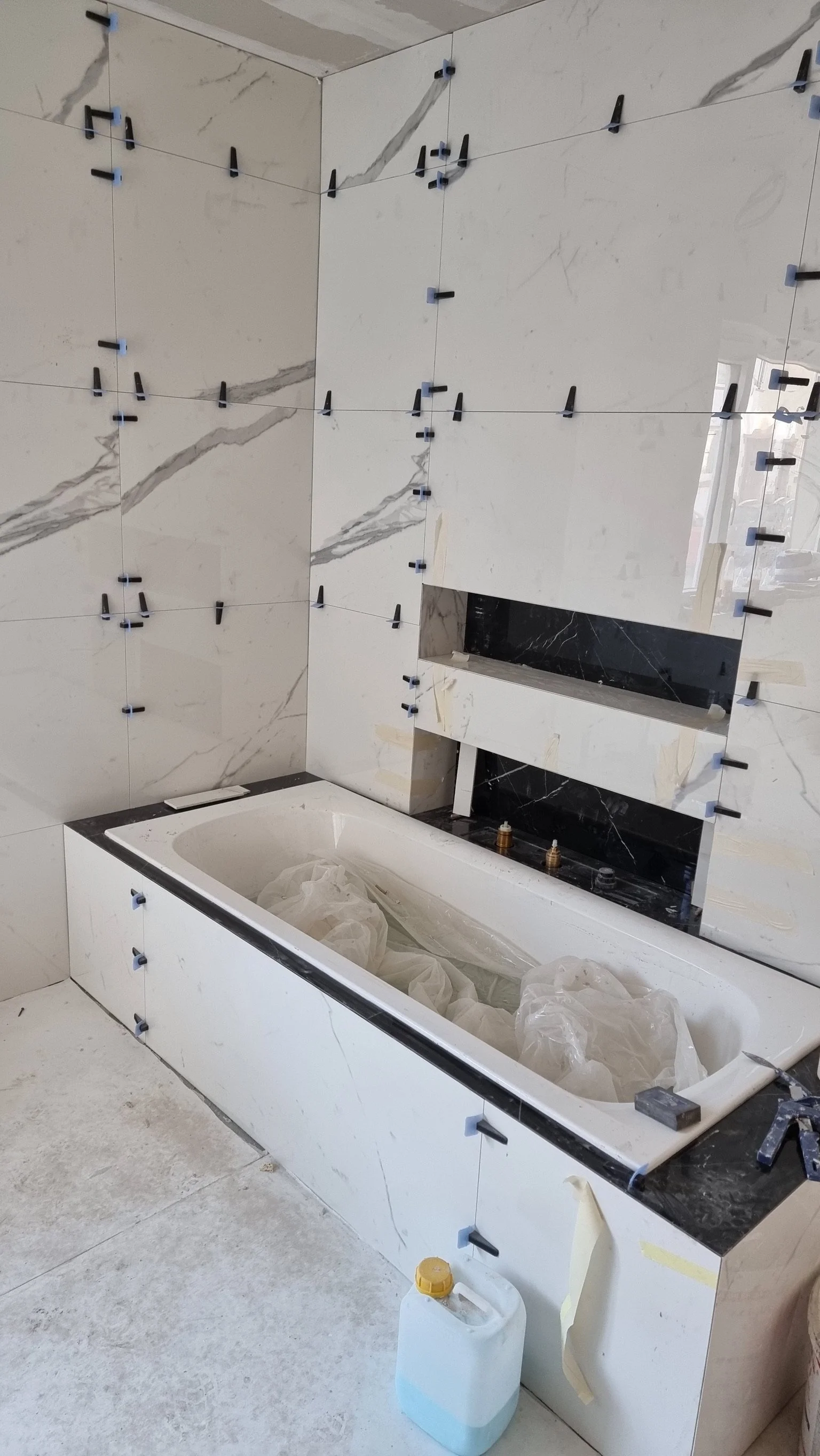 Badezimmer im Bau mit weißen Marmorfliesen, eine Badewanne und sichtbaren Installationsarbeiten.