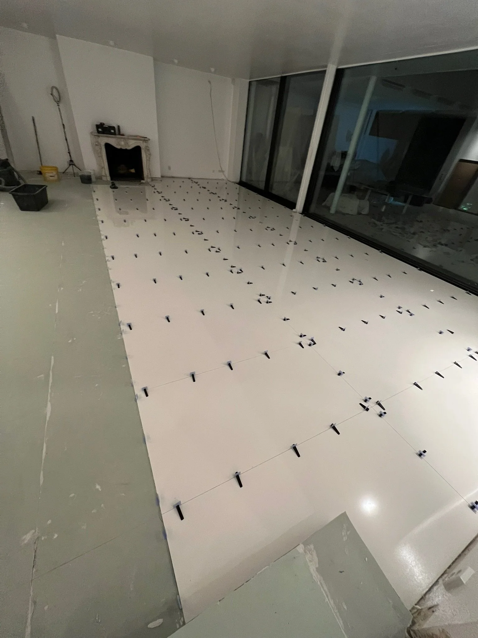 Innenansicht eines Zimmers bei Bodenausbau, mit große weiße Fliesen, die noch verfugt werden müssen, und einige Werkzeuge und Baumaterialien im Hintergrund.