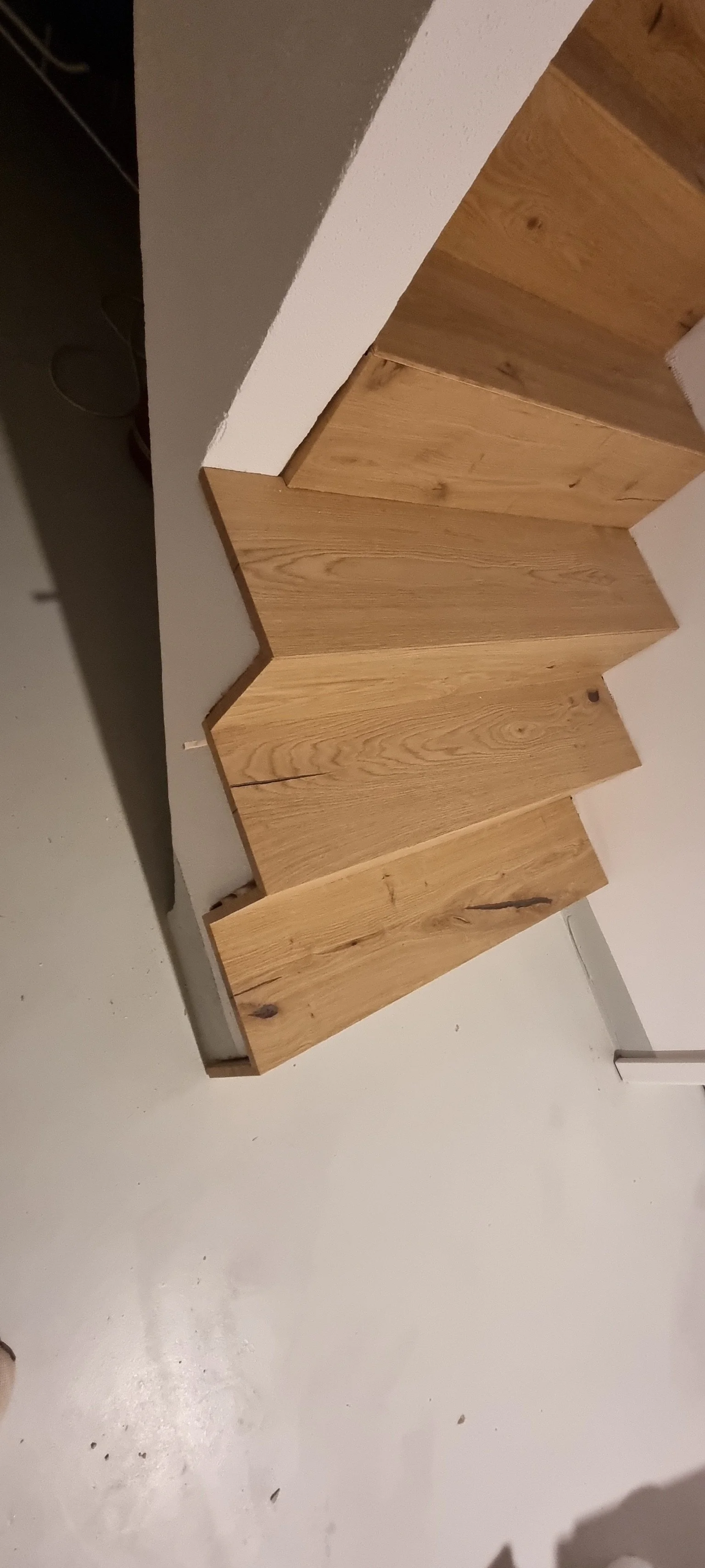 Holztreppe mit einer gezackten Kante, an einer weißen Wand, auf einem weißen Boden