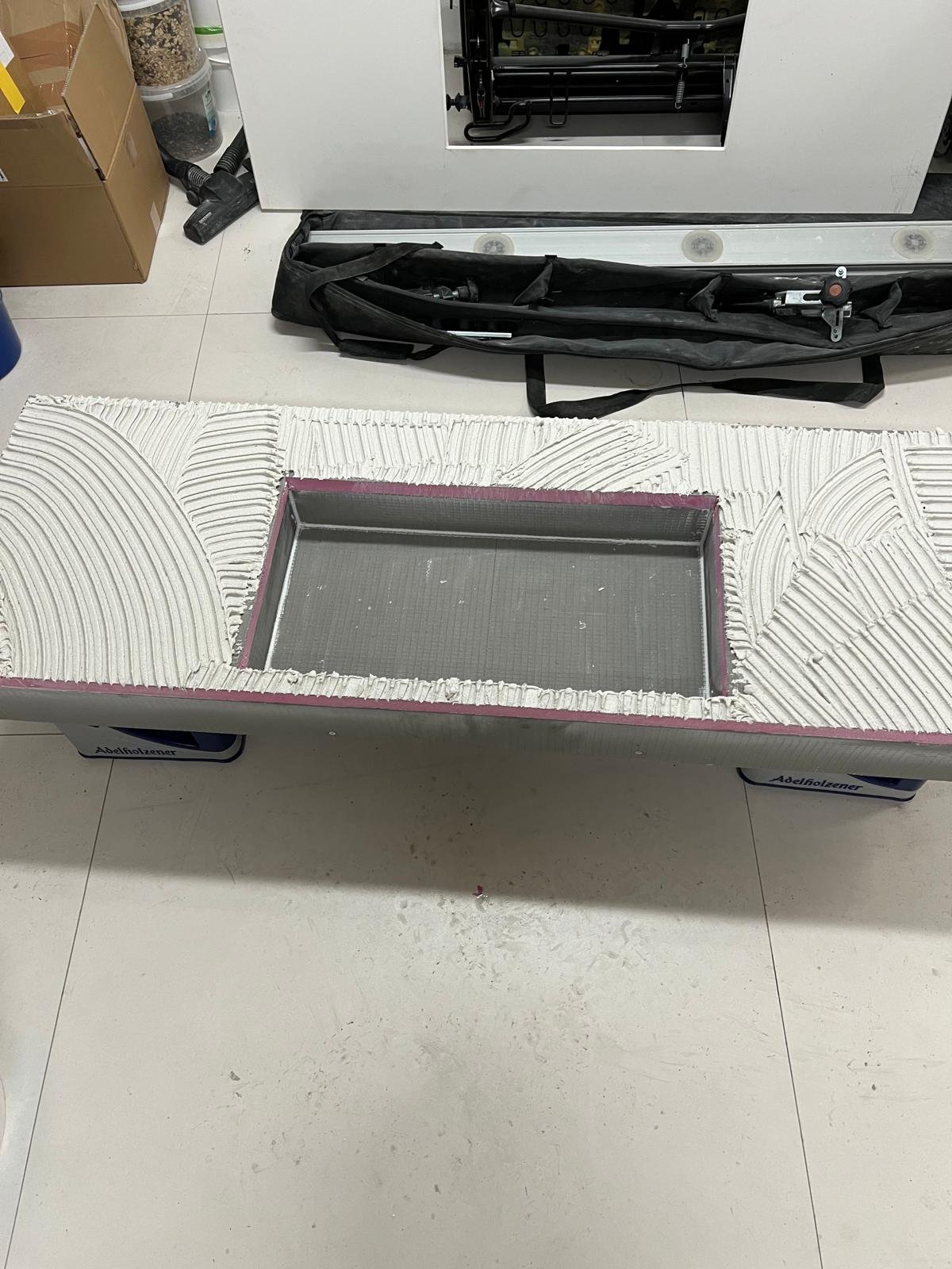 Eine Werkbank mit einer halbfertigen Gießform, umgeben von Baumaterialien und Werkzeugen.