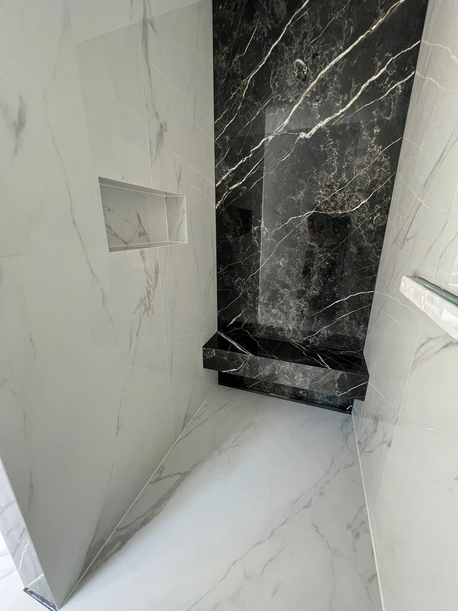 Ein moderner Duschraum mit weißen und schwarzen Marmorfliesen, einer eingebauten Nische in der Wand und einer schwarzen Marmor-Duschtreppe.