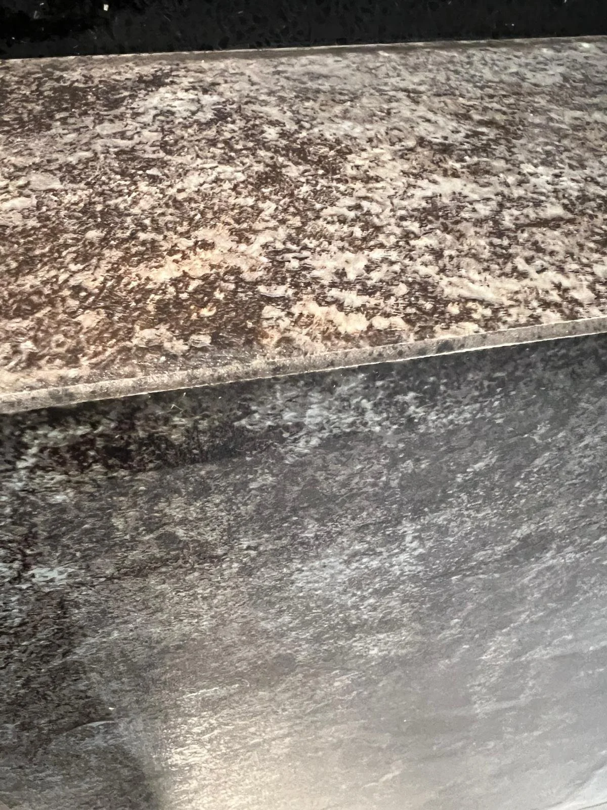 Eine Oberfläche aus dunklem, poliertem Marmor mit einer weiteren, erhobenen Platte aus hellem, strukturiertem Marmor.