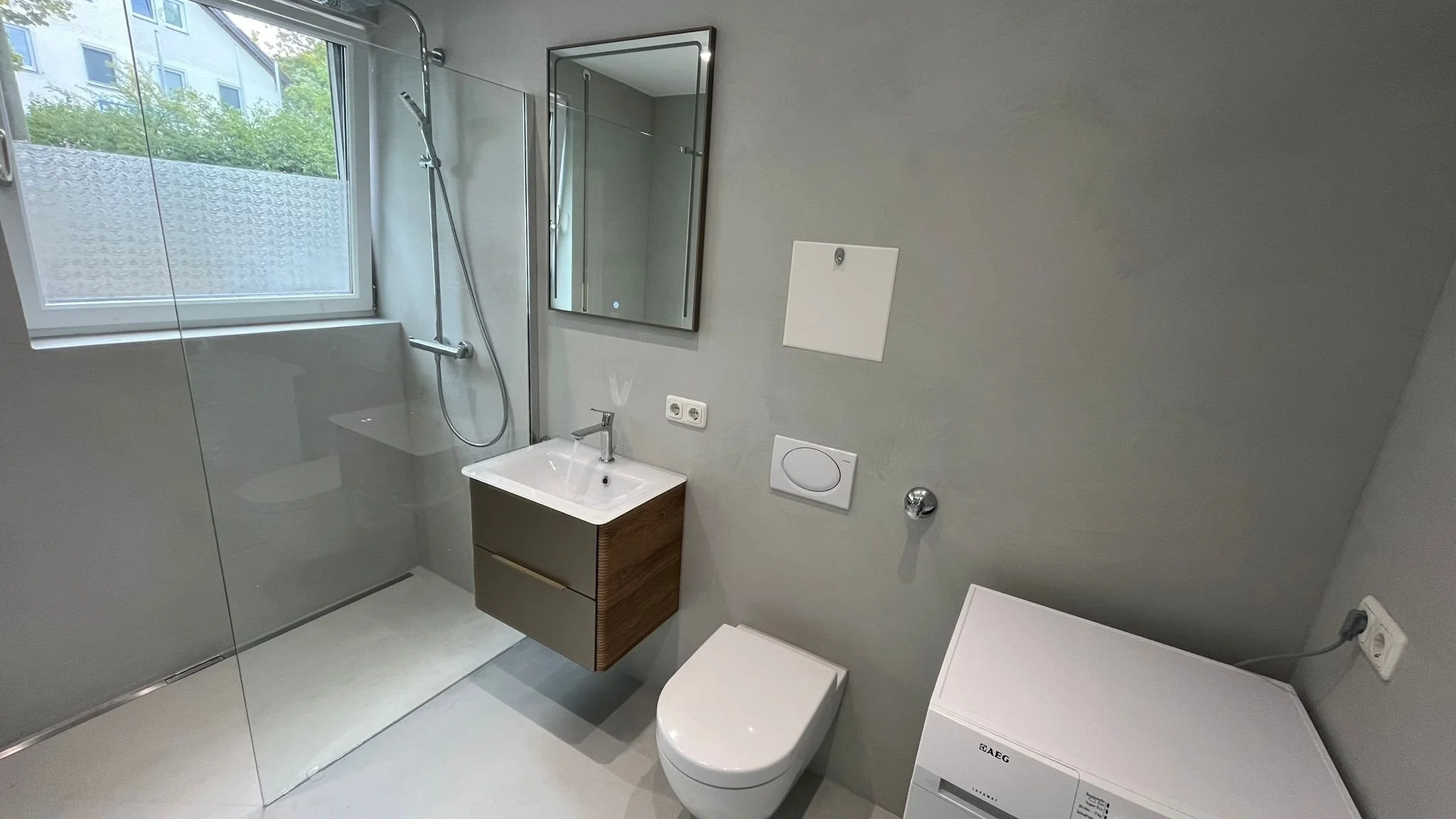 Modernes Badezimmer mit Dusche, Waschbecken, Spiegel, WC und Waschmaschine, Fenster mit Blick nach außen
