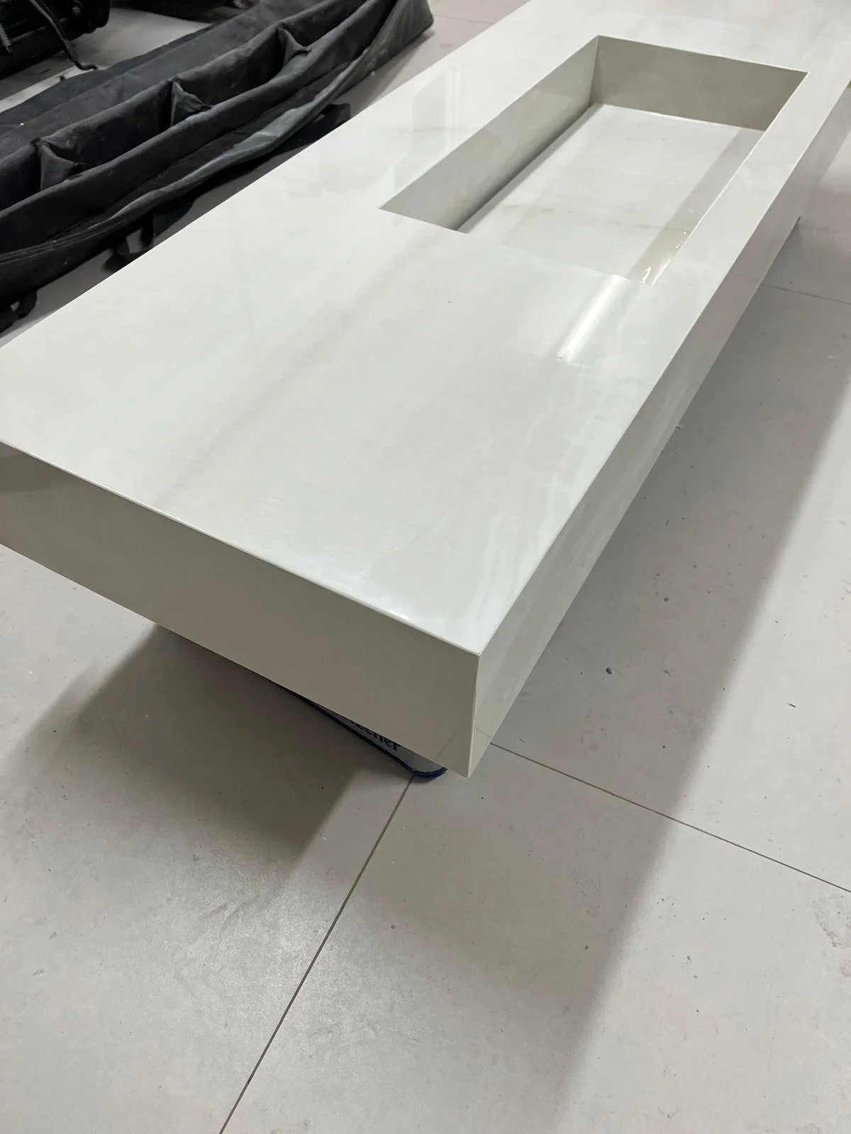 Ein weißer, rechteckiger Waschtisch aus Marmor mit integrierter Ablage und einer ovalen Aussparung, auf einem hellen Fliesenboden.