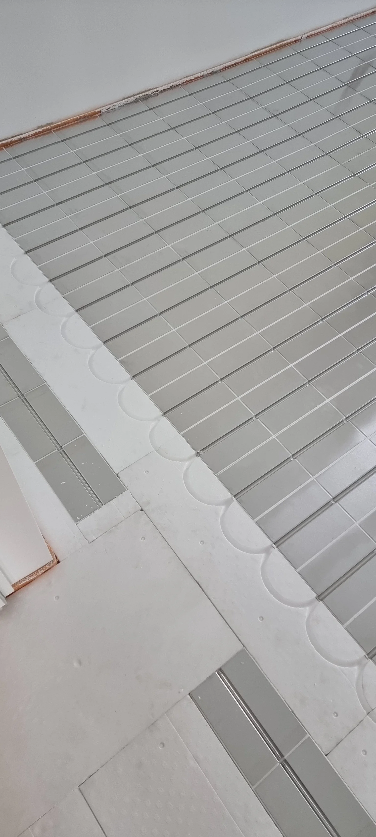 Weiße Fliesen auf dem Boden mit einem Gitter aus grauen Fliesen und einer Ecke, in der Fliesen mit Silikon verfugt werden.