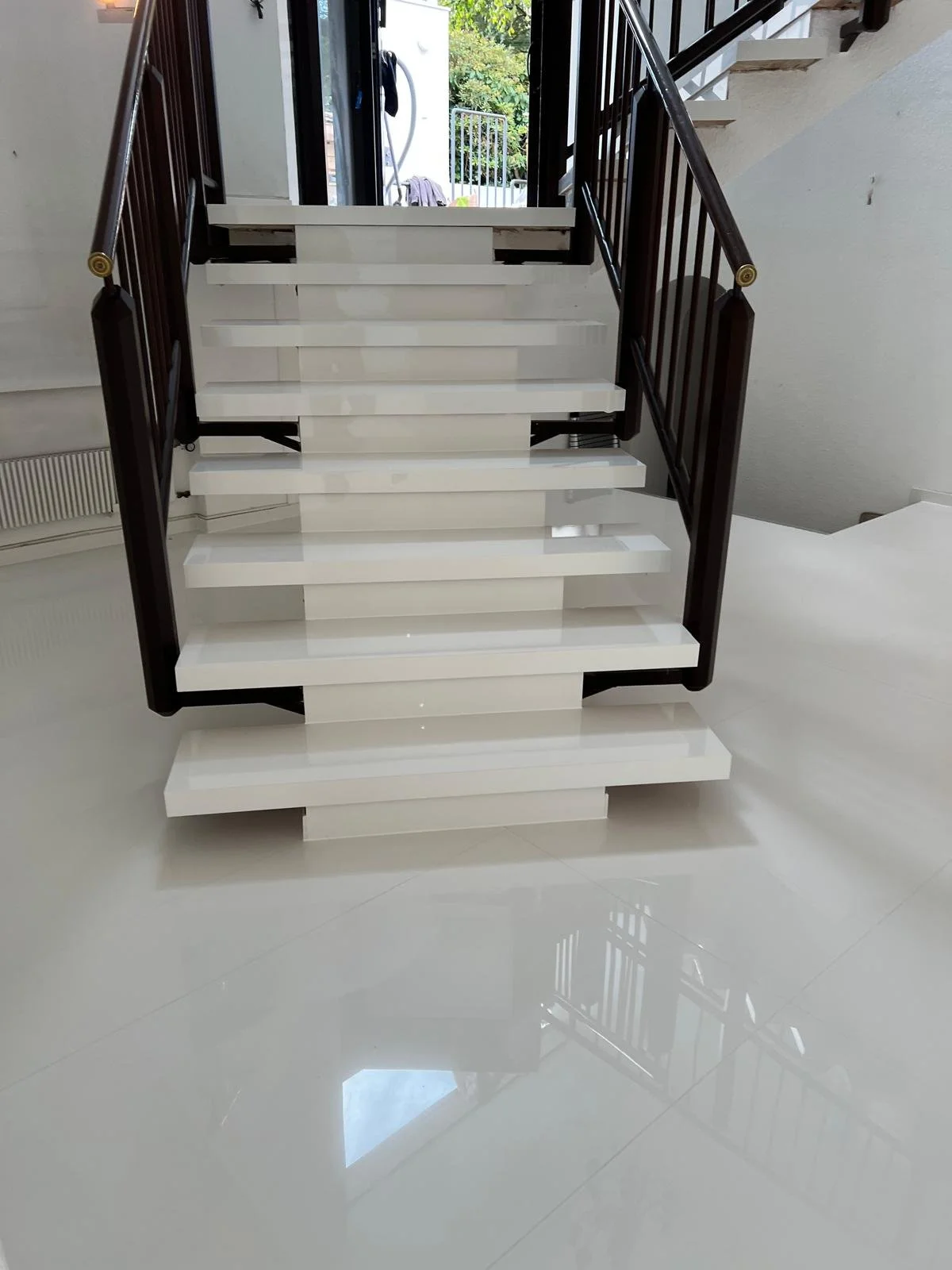 Moderne weiße Treppe mit dunklen Geländern in einem Innenraum, mit Blick nach draußen auf einen Garten.