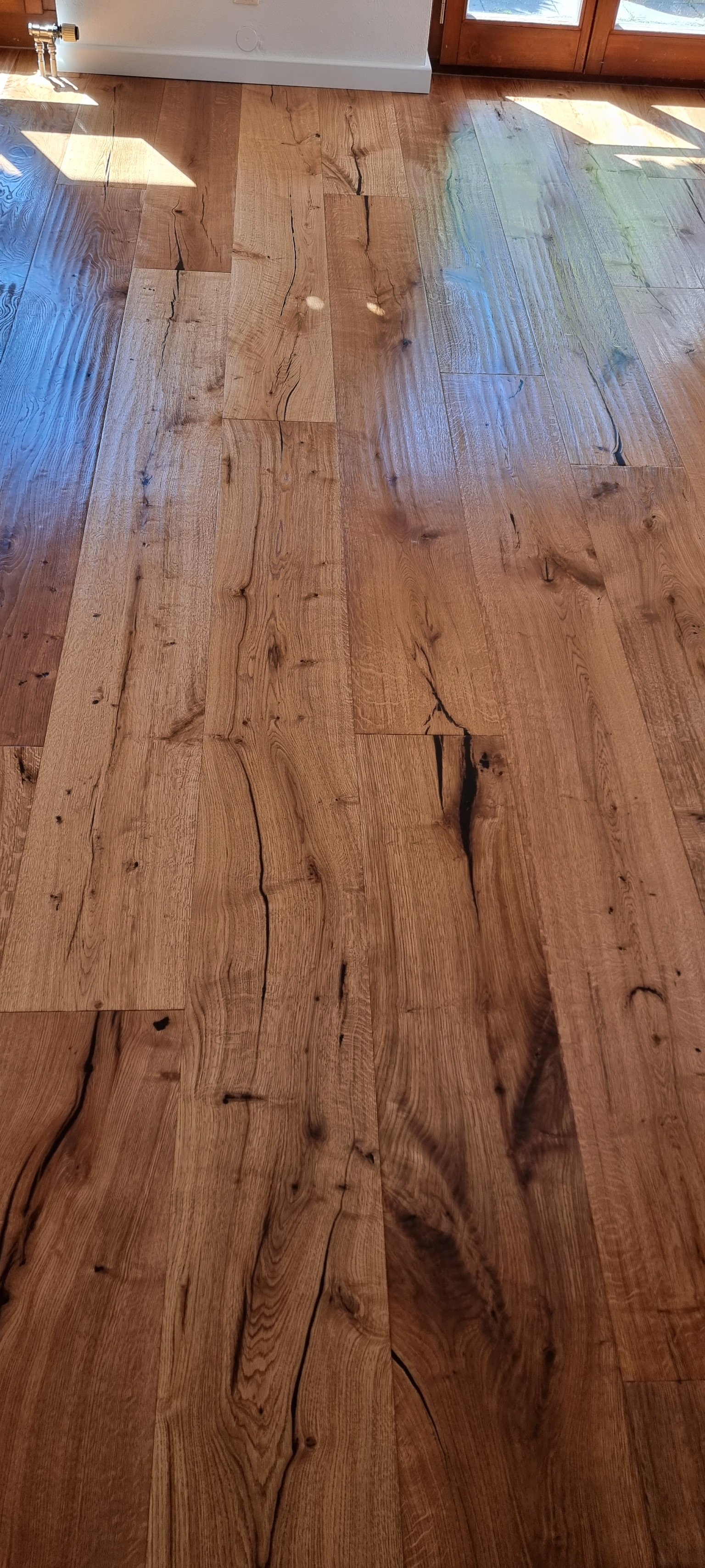 Holzboden mit sichtbaren Knoten und Rissen, teilweise reflektierende Lichtreflexe auf der Oberfläche.