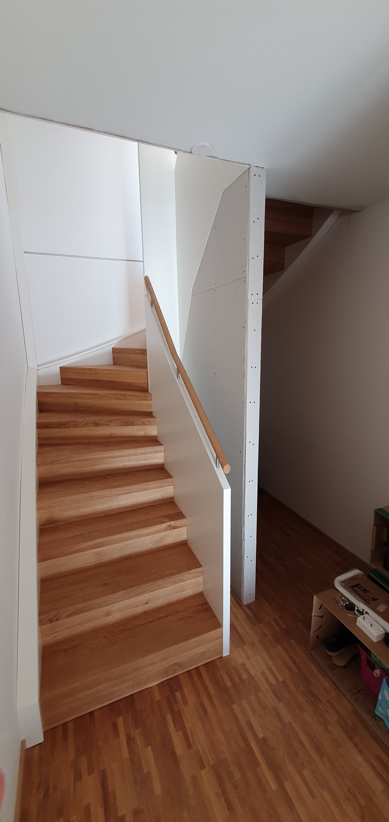 Holztreppe mit weißer Seitenverkleidung und Handlauf aus Holz in einem modernen Haus unter einer Dachschräge.