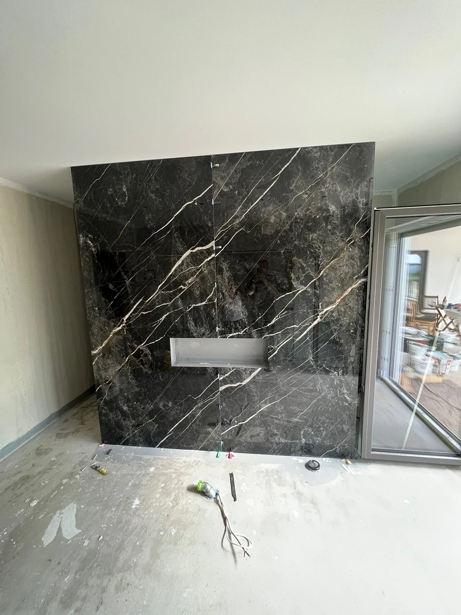 Schwarze Marmorwand mit weißen und goldenen Adern in einem Raum, der gerade renoviert wird, mit sichtbaren baulichen Elementen und Kabeln auf dem Boden.