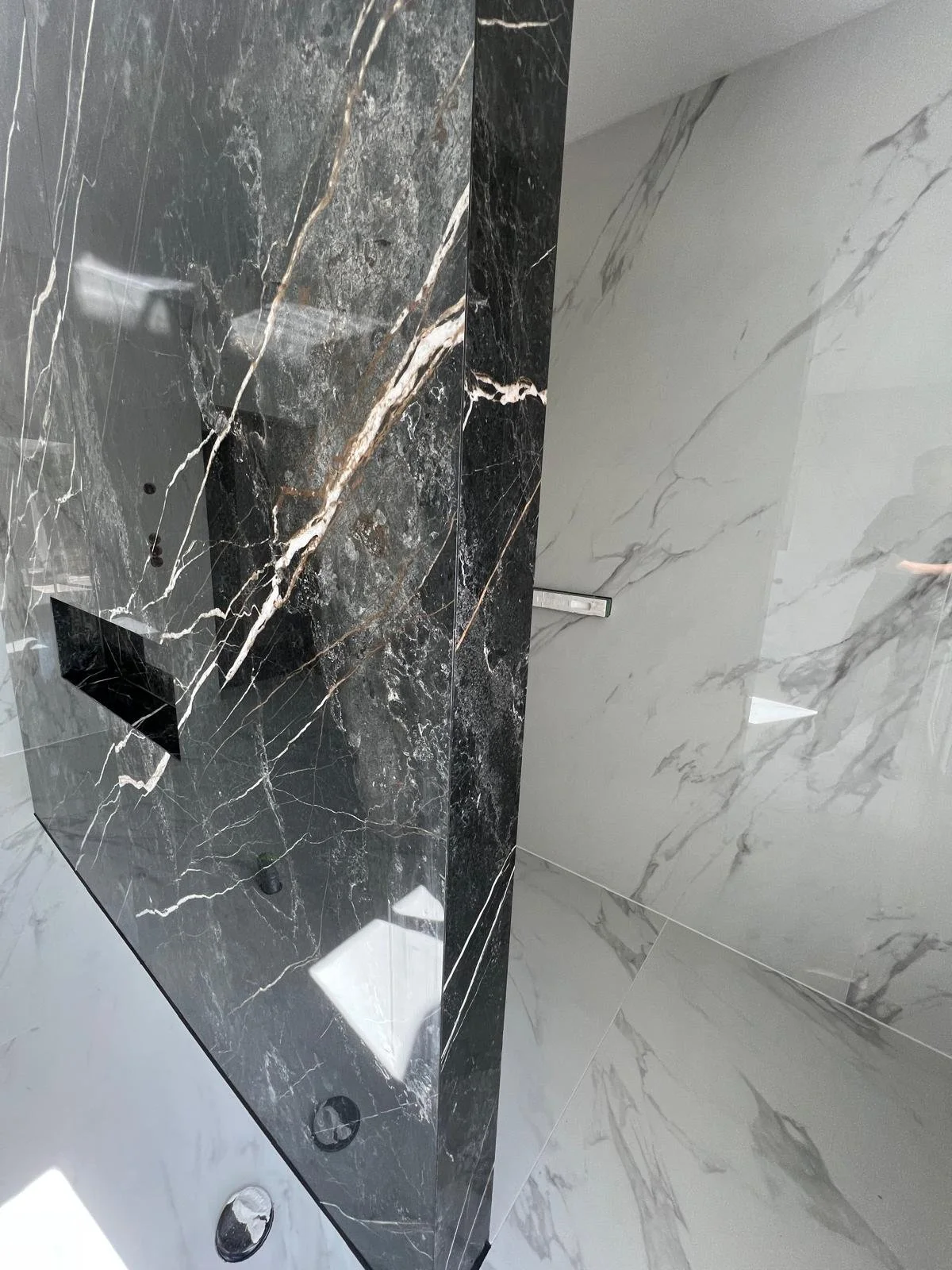 Innenansicht eines modernen Badezimmers mit einer schwarzen Marmorwand und weißen Marmorfliesen auf dem Boden und an der Wand.