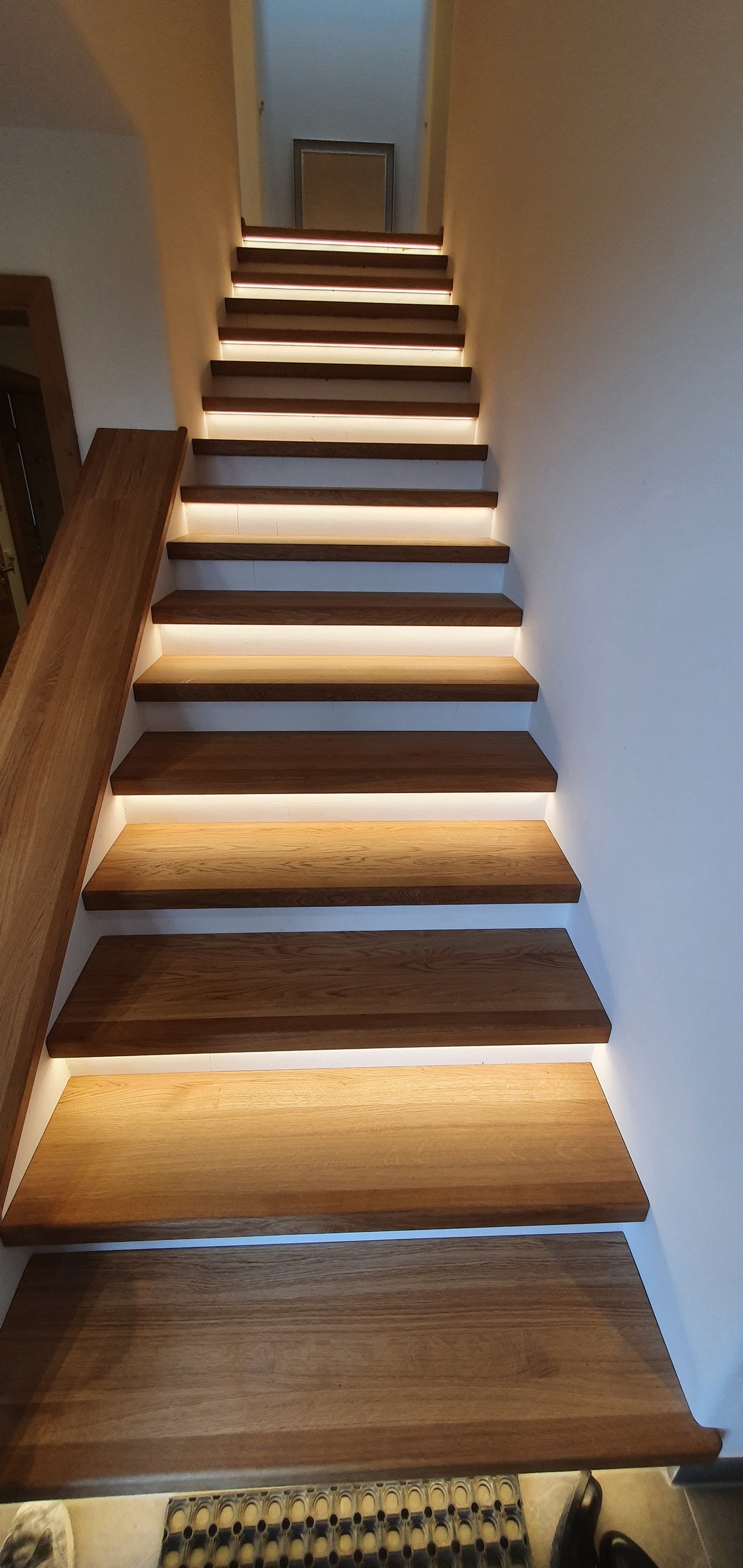 Holztreppe mit LED-Beleuchtung an den Tritten, Innenaufnahme mit weißen Wänden.